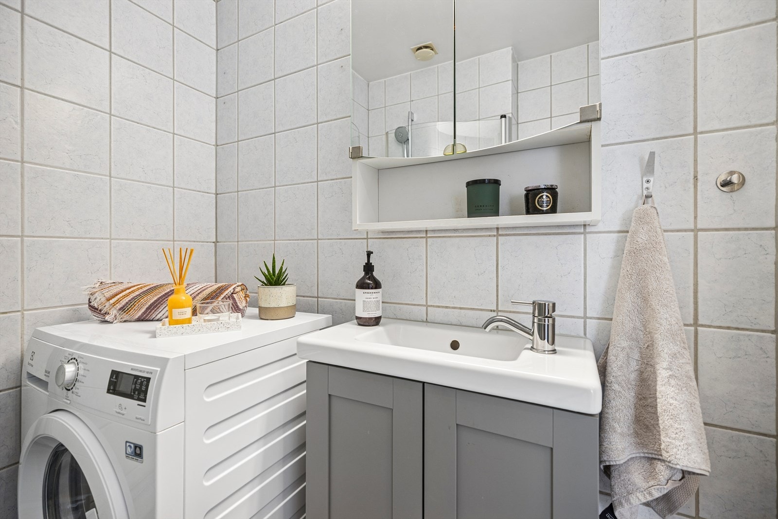 Leiligheten har et delikat flislagt baderom oppusset av borettslaget. Baderomsinnredningen består av nyere servant med underskap, speilskap med overlys, nyere klosett, dusjhjørne med svingbare glassdører og opplegg for vaskemaskin. Galleribilde