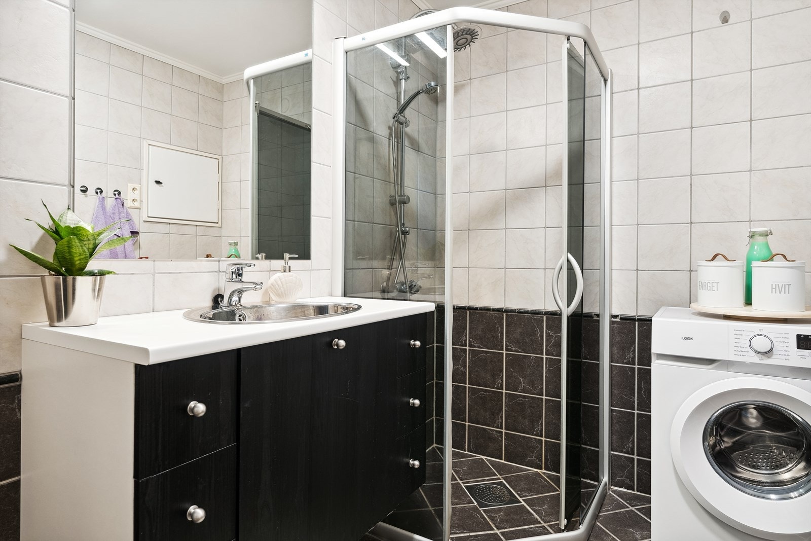 Flislagt bad som inneholder servant med underskap, dusjhjørne, opplegg til vaskemaskin og toalett. Galleribilde