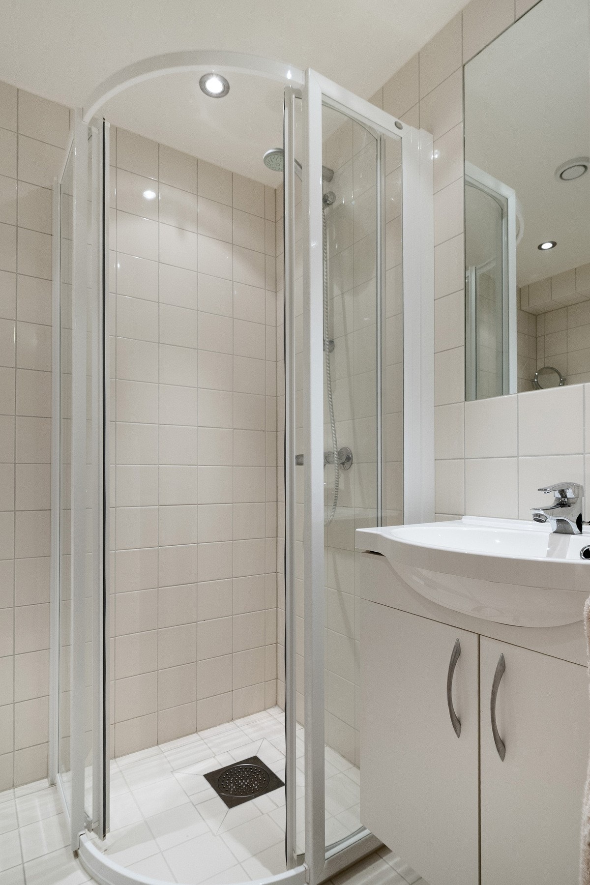 Dusjhjørne med dører og vegghengt dusjarmatur. Vegghengt toalett og mekanisk avtrekk med ventil i himling. Galleribilde