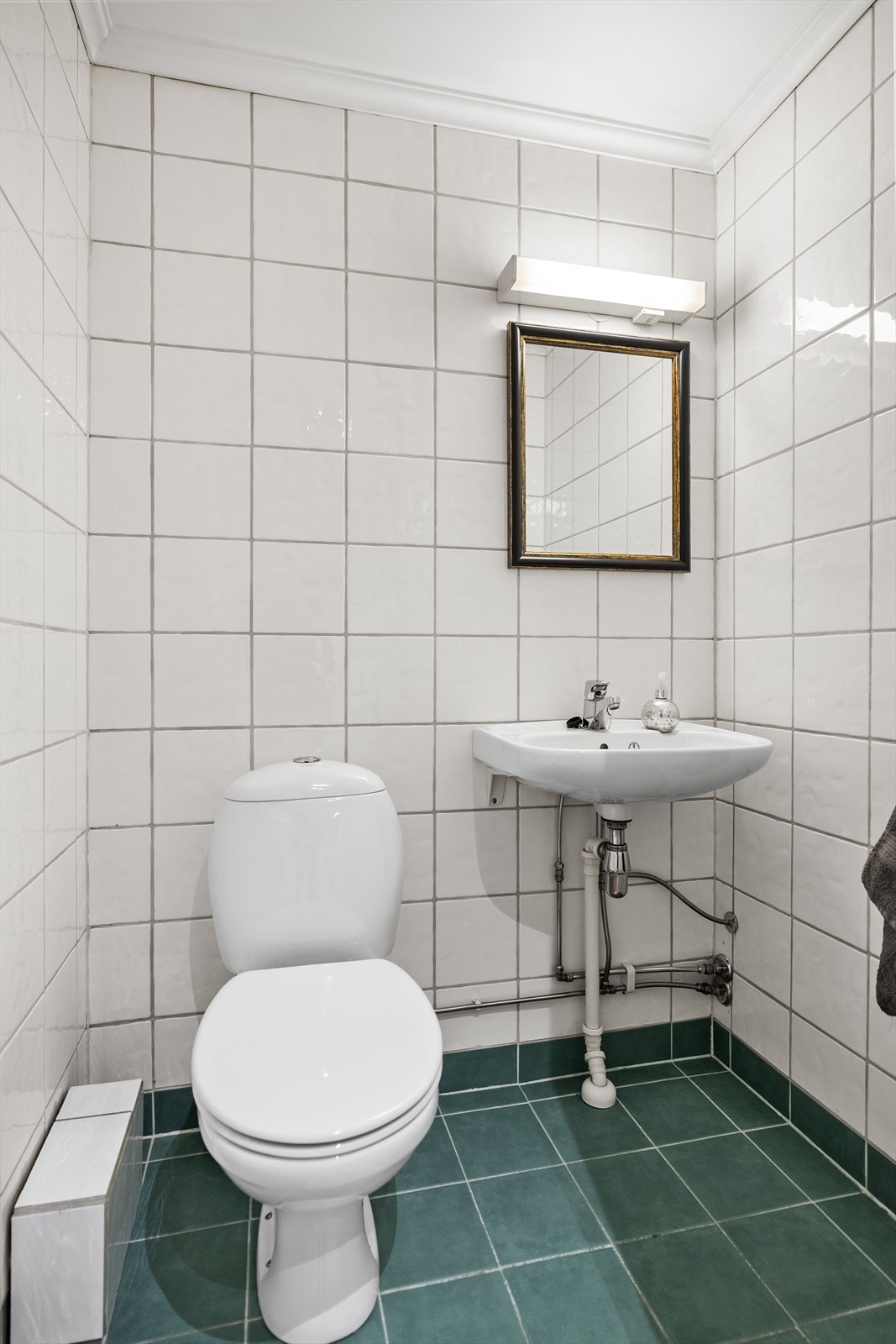 Toalettrom med flislagt gulv, flislagte vegger og malt tak. Rommet er innredet med toalett og servant. Galleribilde