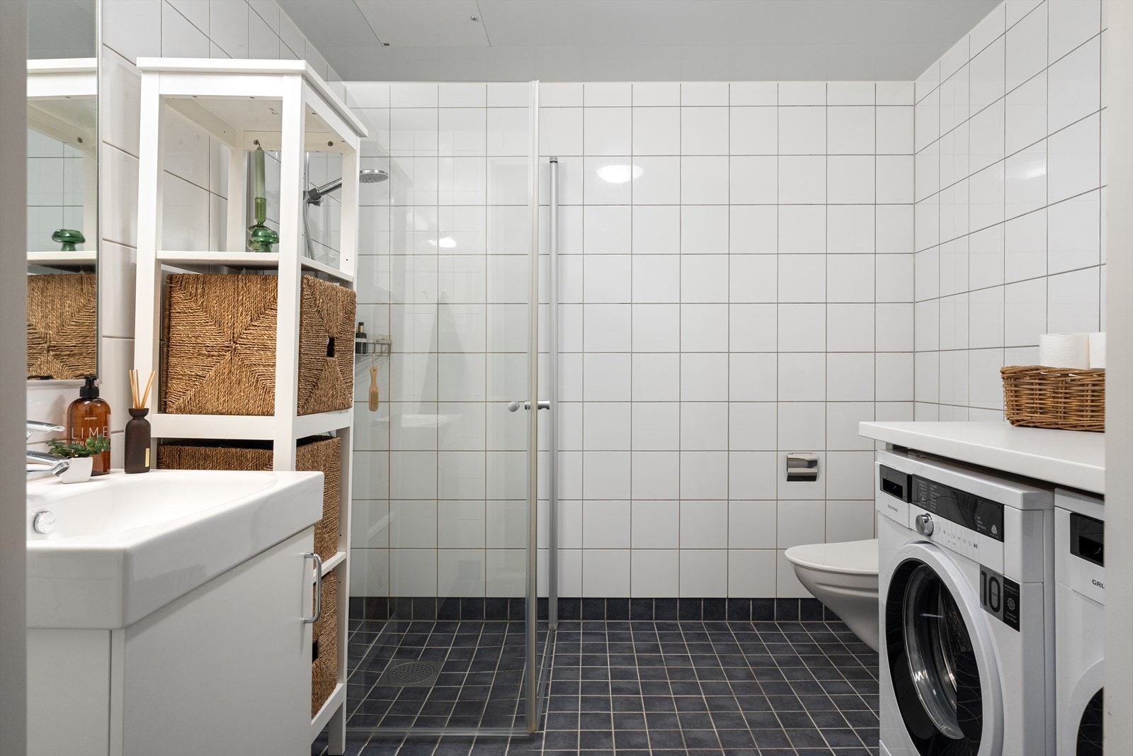 Helfliset bad med gulvvarme innredet med vegghengt toalett, benkeskap med servant, dusjdører i glass og opplegg for vaskemaskin. Galleribilde