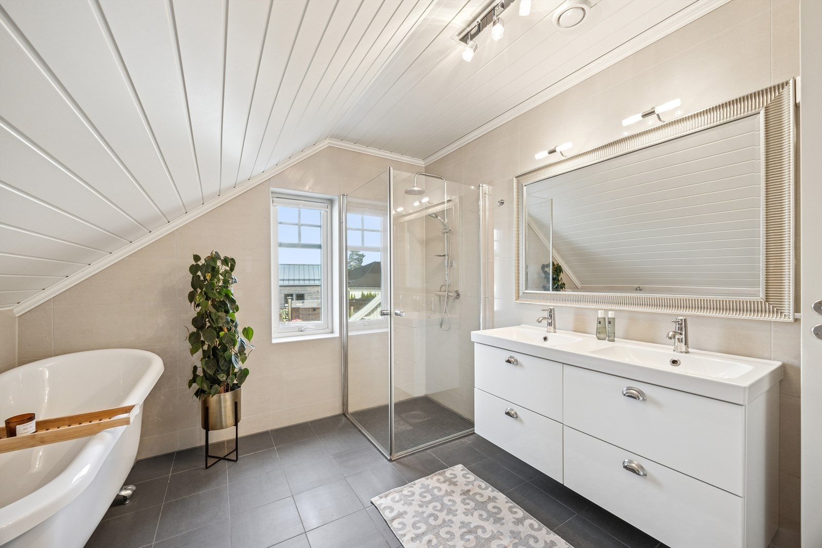 Badet i andre etasje fremstår moderne og innbydende, med baderomsinnredning i høyglanset utførelse og glatte fronter. To servanter er integrert i en helstøpt plate, med speil og belysning over som gir både god funksjonalitet og et stilrent uttrykk. Galleribilde