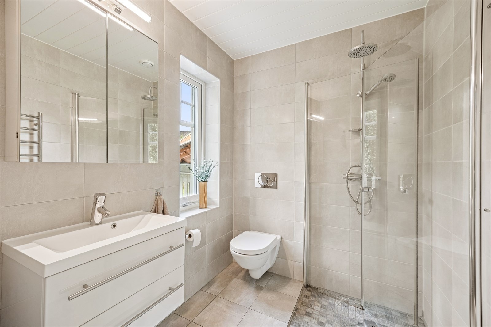 Lekkert og helfliset bad med moderne baderomsinnredning i høyglanset utførelse. Benkeskap med glatte fronter gir et stilrent uttrykk, mens veggskap med speilfronter og integrert belysning gir både funksjon og eleganse. Galleribilde