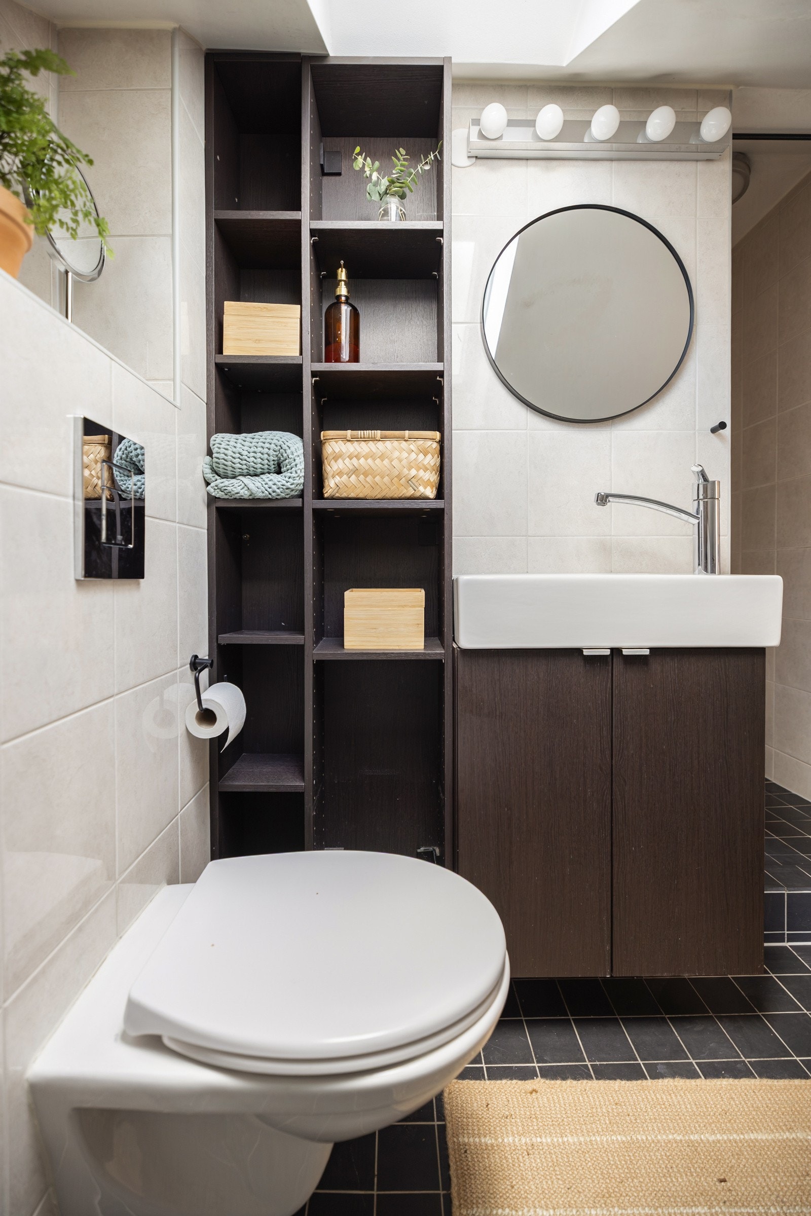 Stilig baderomsinnredning, med servantskap og ovenpåliggende servant med ett-greps armatur. Rundt veggspeil. Baderommet er også utstyrt med dusjhjørne med hånddusj samt vegghengt toalett. Galleribilde