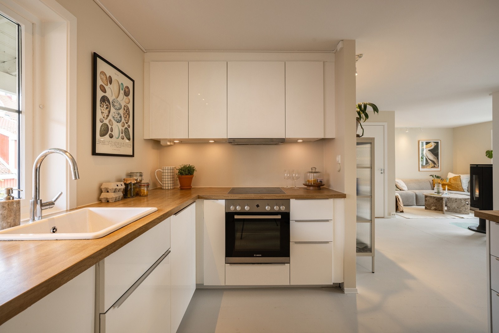 Kjøkkeninnredningen er stilren og tidløs, med hvite, glatte fronter og tre benkeplate med underlimt oppvaskkum og ett-greps armatur. Galleribilde