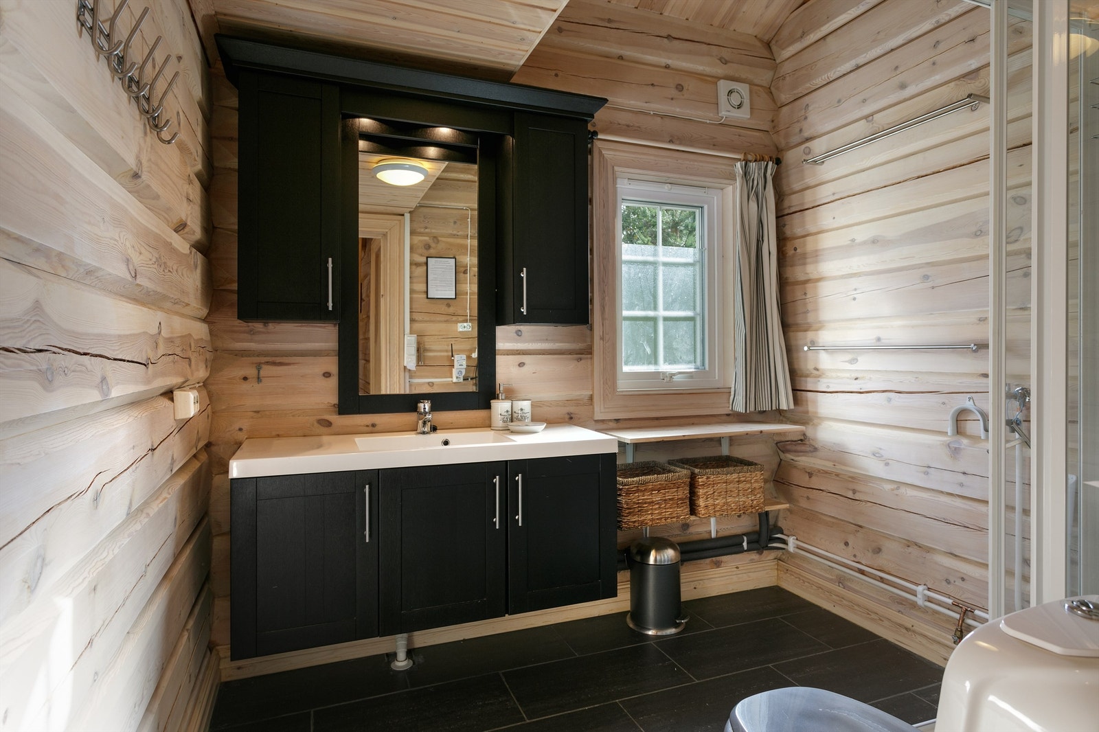 Flislagt gulv med varmekabler, vegger i panel/tømmer og panel i tak. Baderomsinnredning med servant, toalett og dusjkabinett. Opplegg for vaskemaskin. Galleribilde