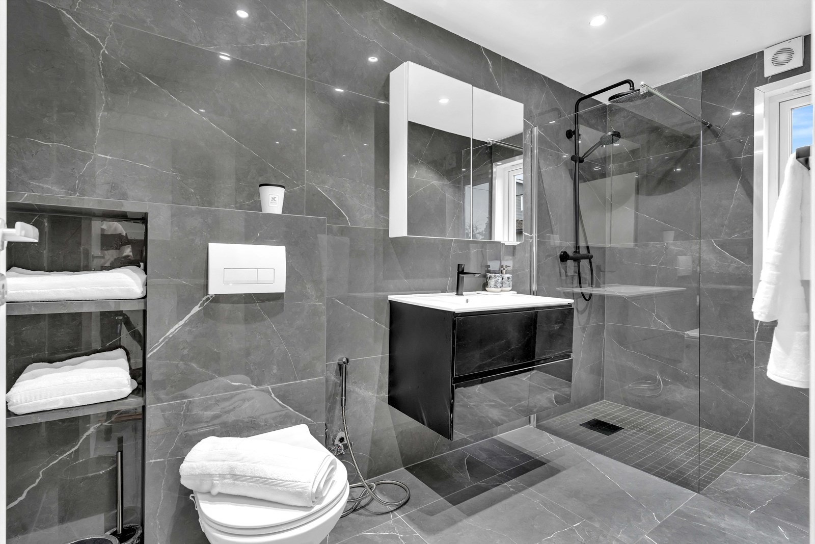 Lekkert bad innredet med regnfallsdusj, toalett, servant og veggskap med speil. Galleribilde