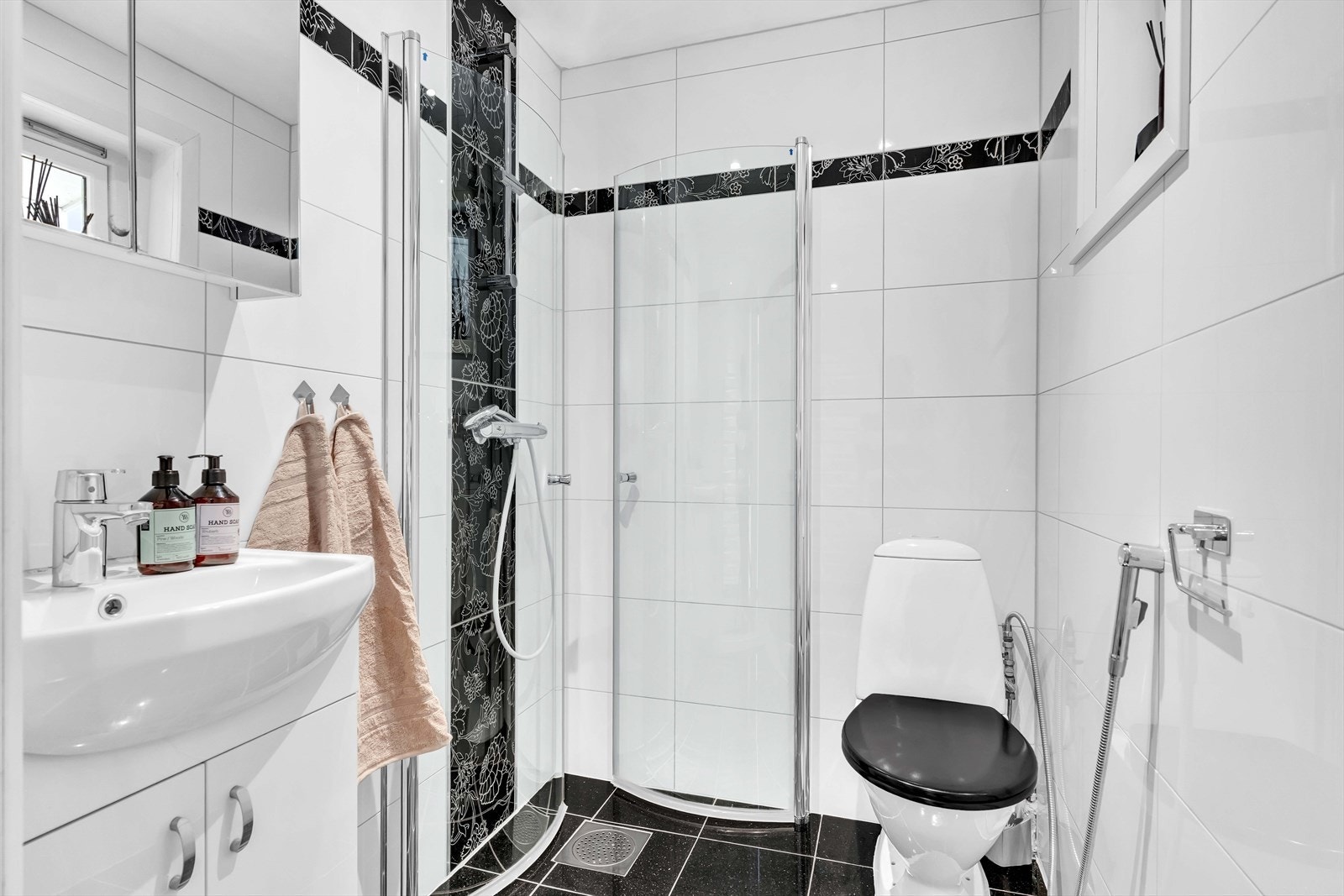 Badet er innredet med fliser på gulv og vegger, toalett, dusjhjørne, servant og veggskap med speil. Galleribilde