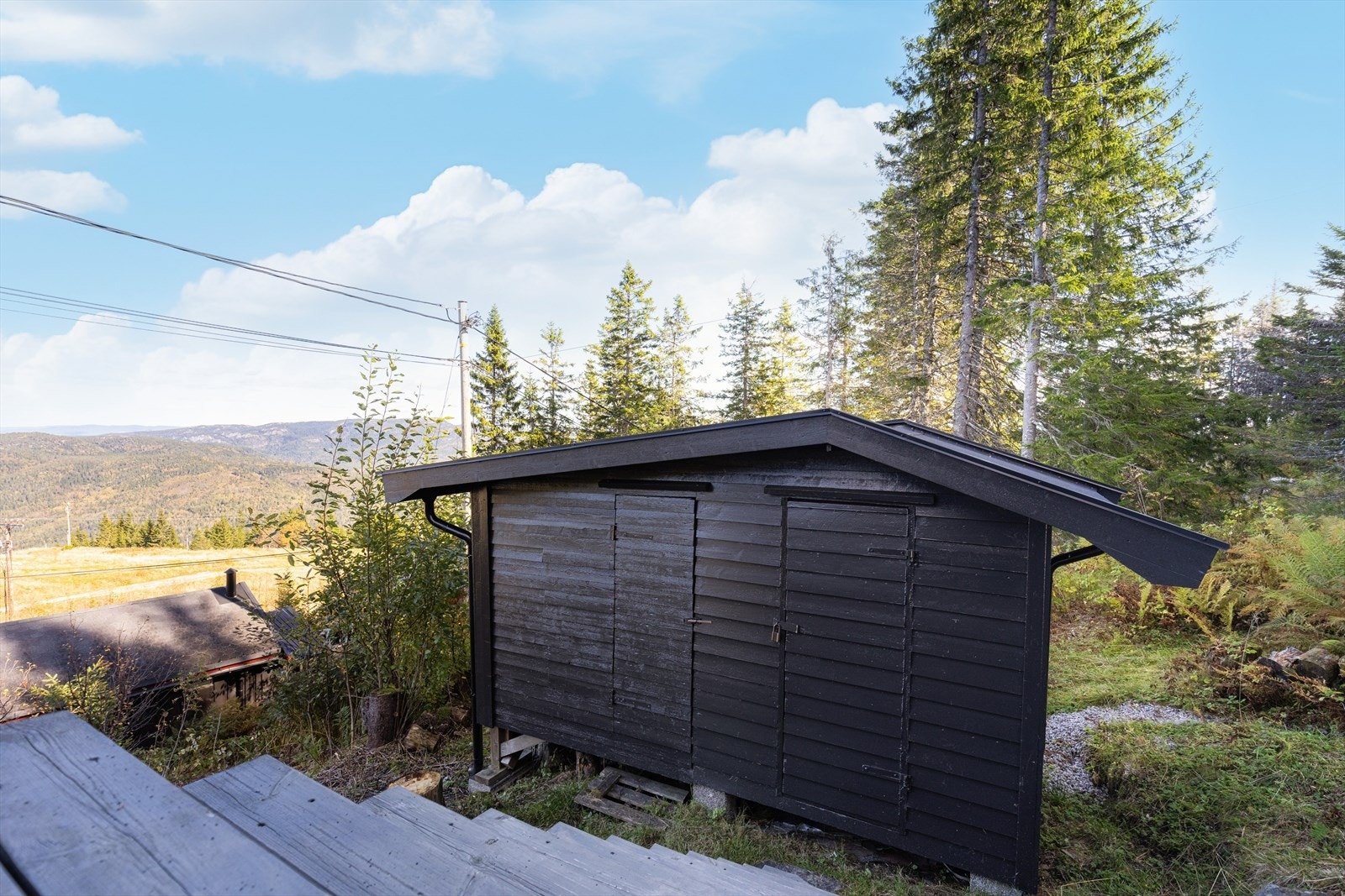 Trapp fra veranda til terreng, hvor det er oppført en frittstående bod. Halvparten benyttes som vedbod, og den andre halvparten som skibod. Galleribilde