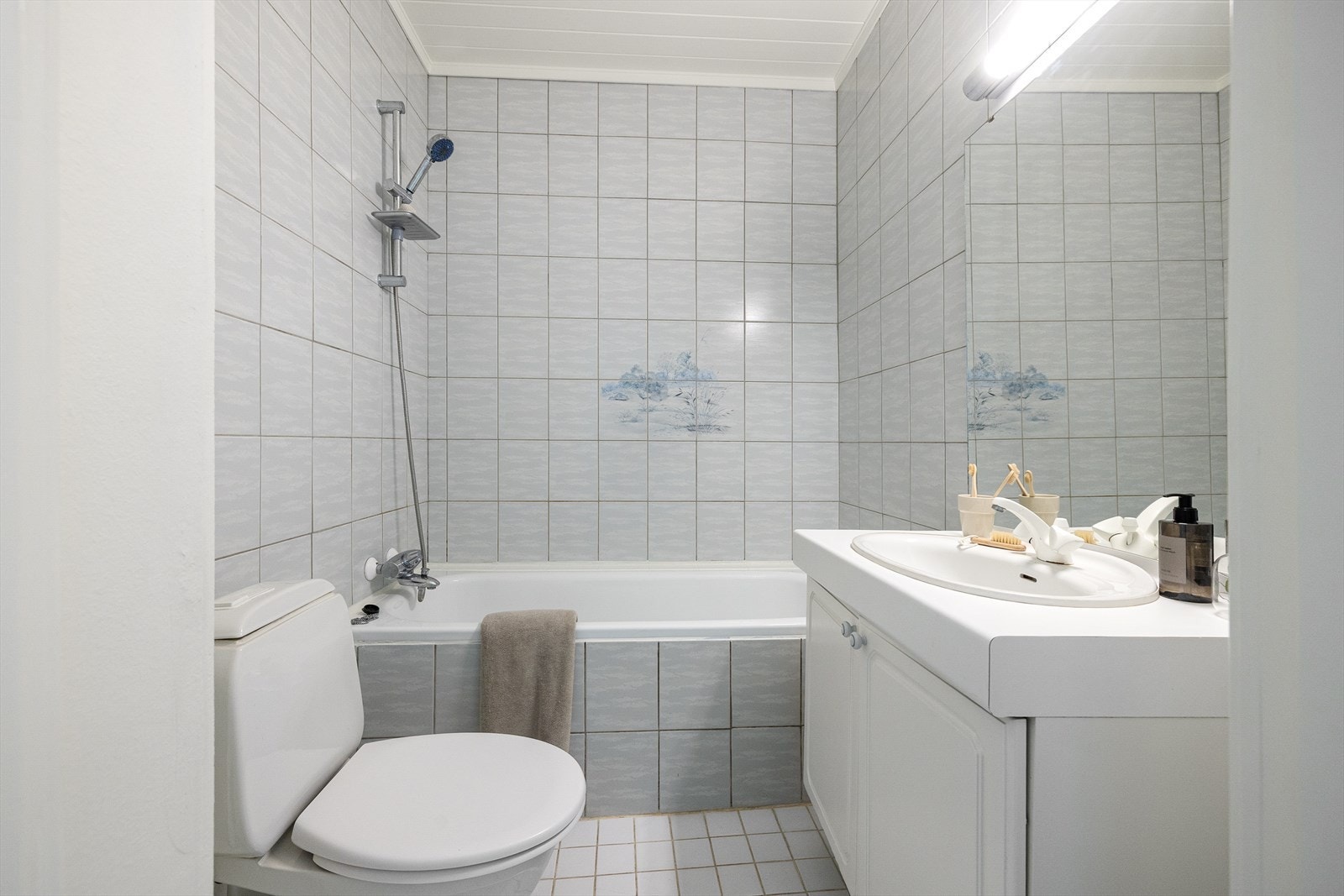Badet er helfliset på både gulv og vegger, og har innredning med badekar, toalett og servant med oppbevaing i underskap. Galleribilde