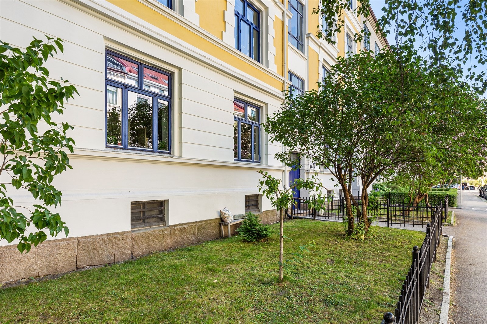 Pent opparbeidet forhage med plen og prydbusker - inngjerdet med sort smijernsgjerde. Galleribilde