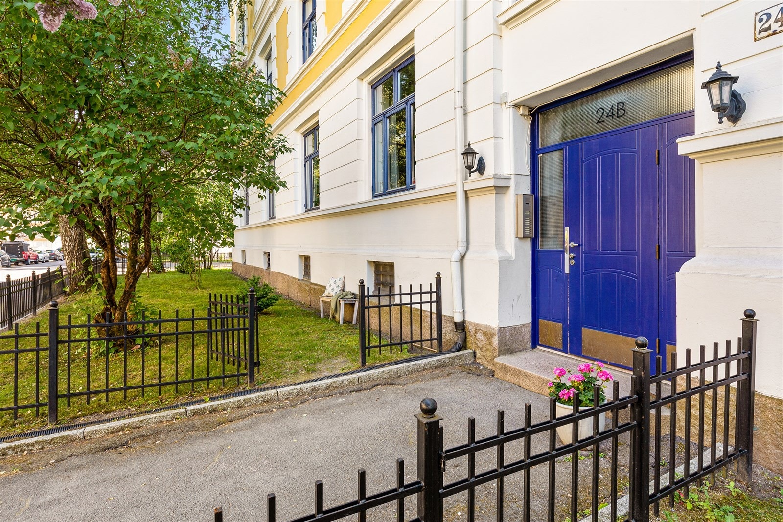 Pent opparbeidet forhage med plen og prydbusker - inngjerdet med sort smijernsgjerde. Galleribilde