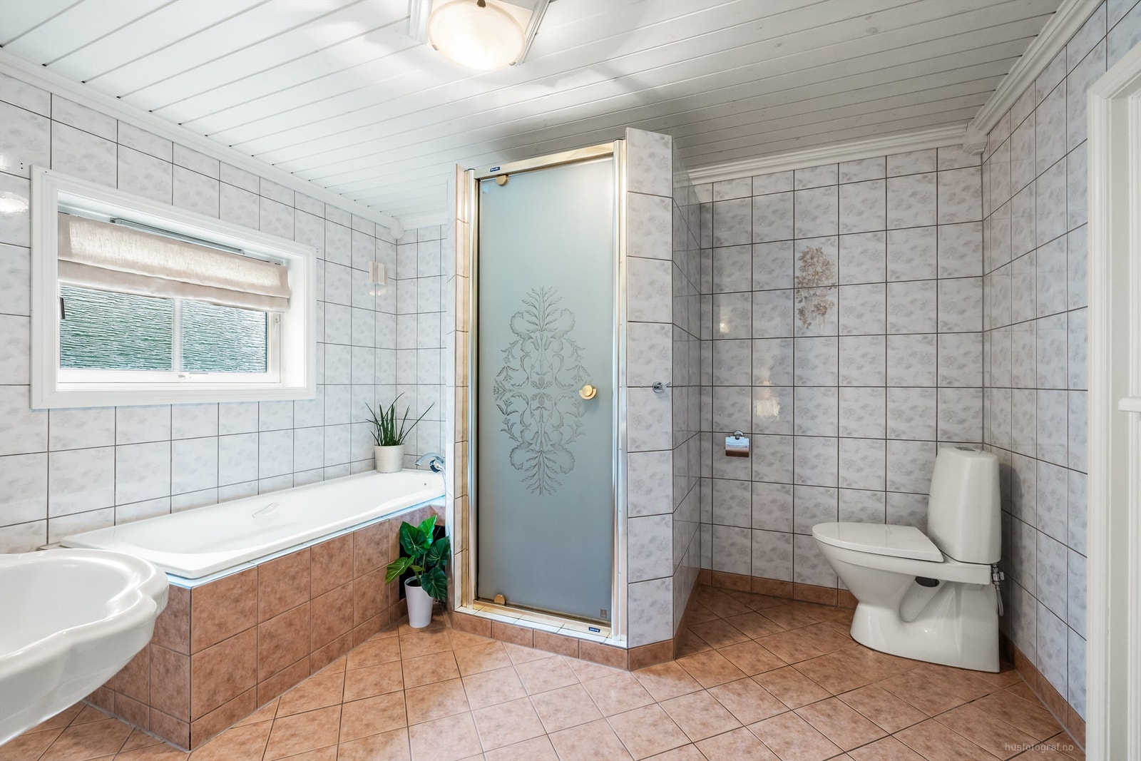 Badet er innredet med badekar, gulvstående toalett og dusj Galleribilde