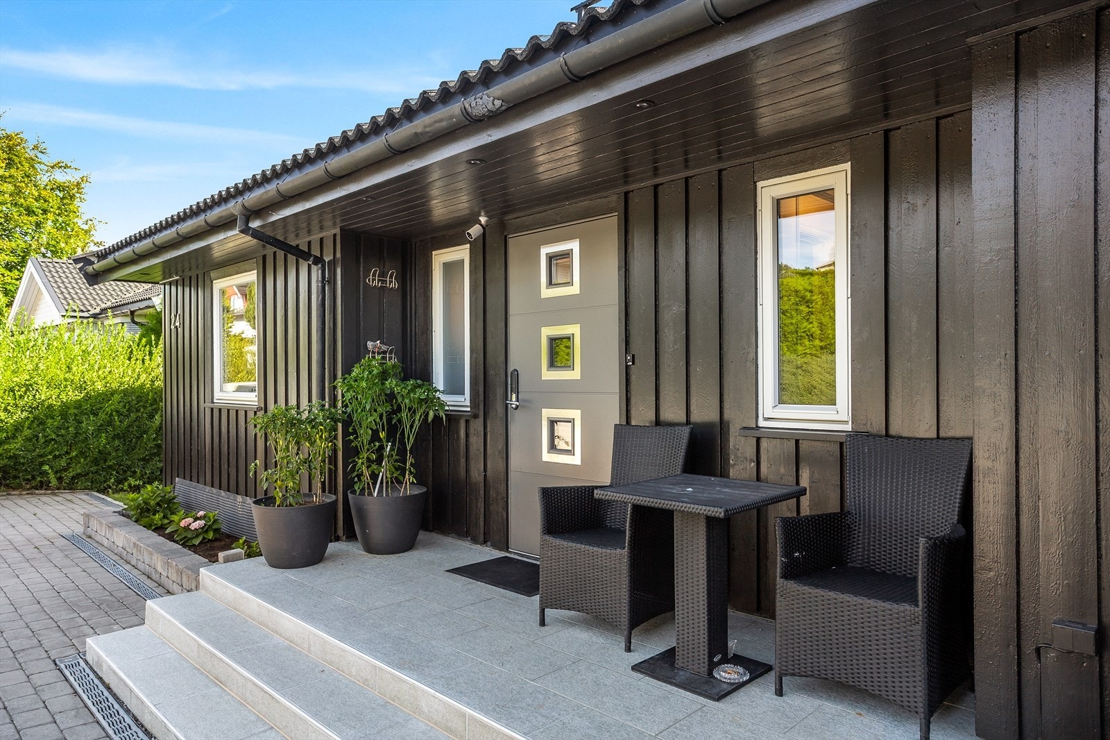 Stilren, mørk fasade og et innbydende, flislagt inngangsparti. Galleribilde