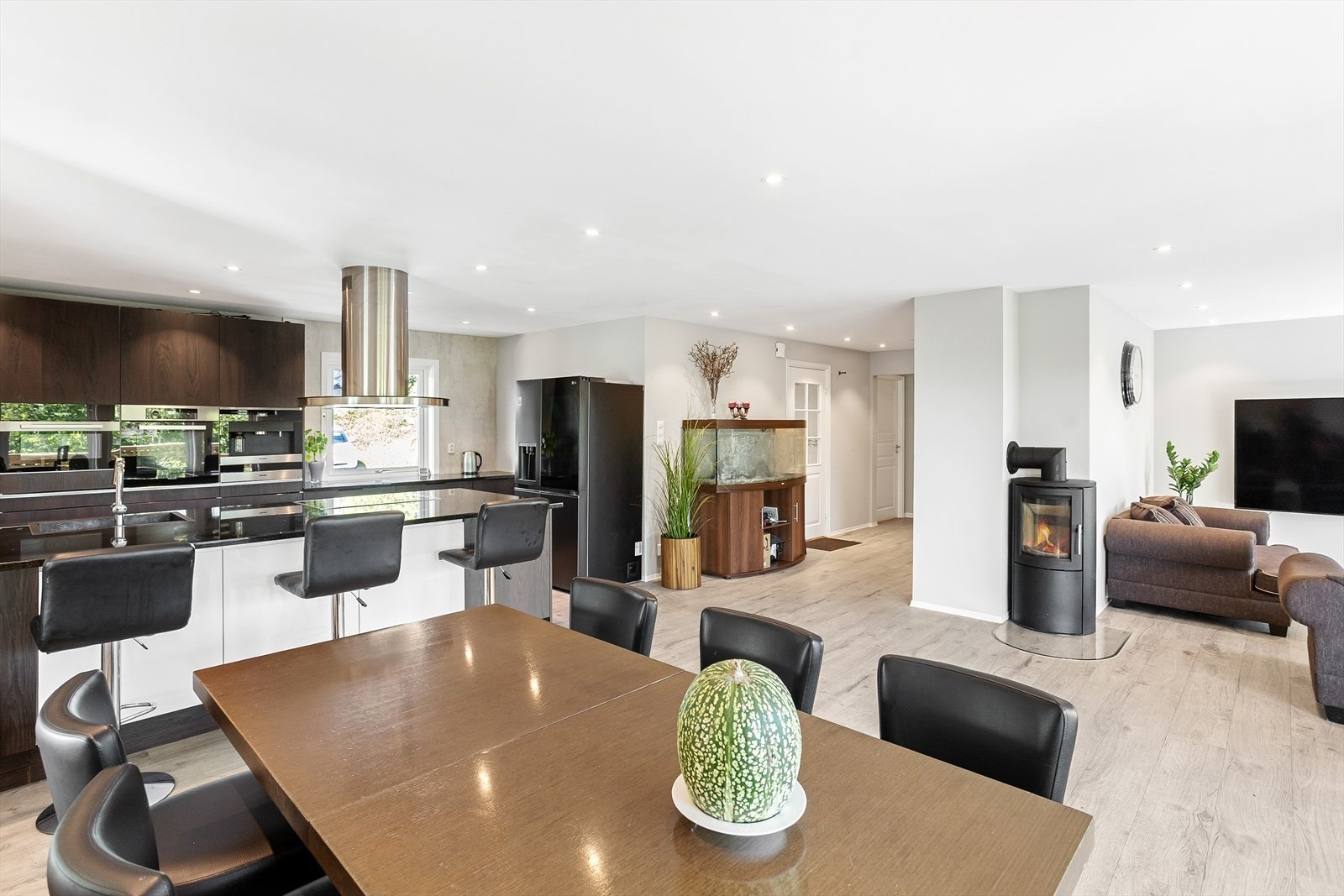 Åpen og sosial sone med stilren kjøkkenøy og lun peisovn. Galleribilde