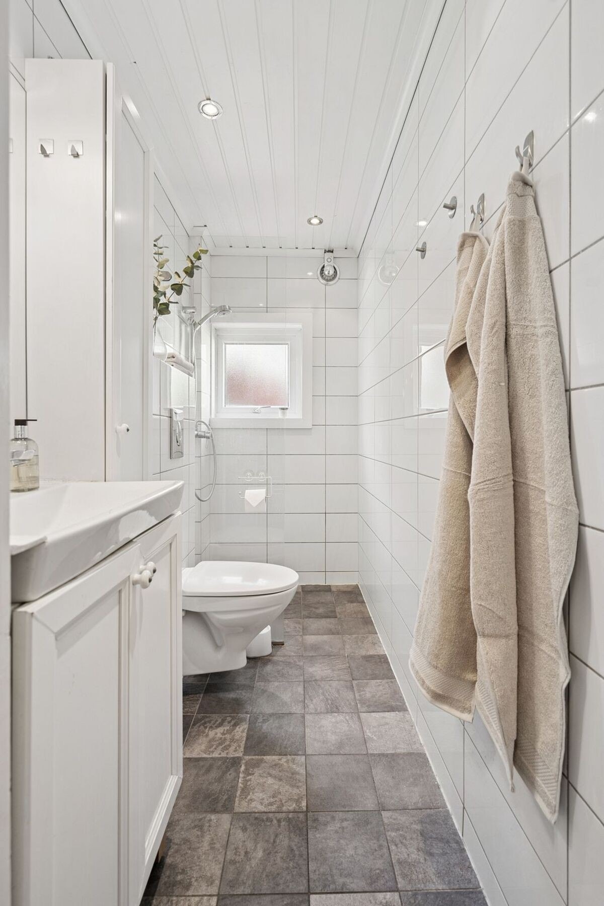 Leiligheten har et pent flislagt bad med hvit innredning og høyskap, dusj og vegghengt wc. Downlights i tak og et lite vindu bidrar til godt med lys i rommet. Galleribilde