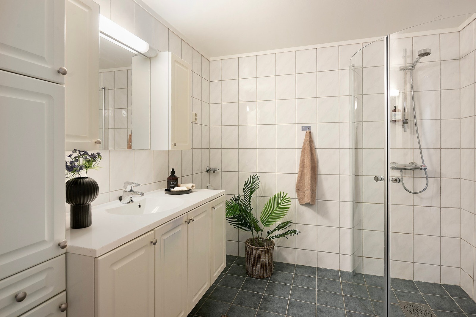 Flislagt bad med dusjhjørne, servant i innredning med god skapplass, og toalett Galleribilde