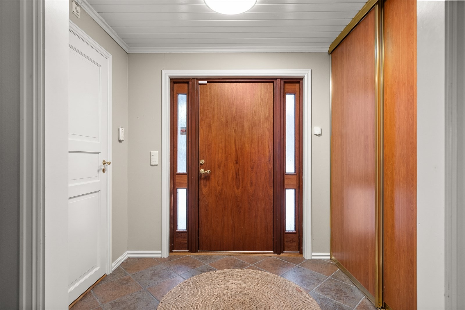 Flislagt entré med god plass til sko og klesavheng i praktisk skyvedørsgarderobe Galleribilde