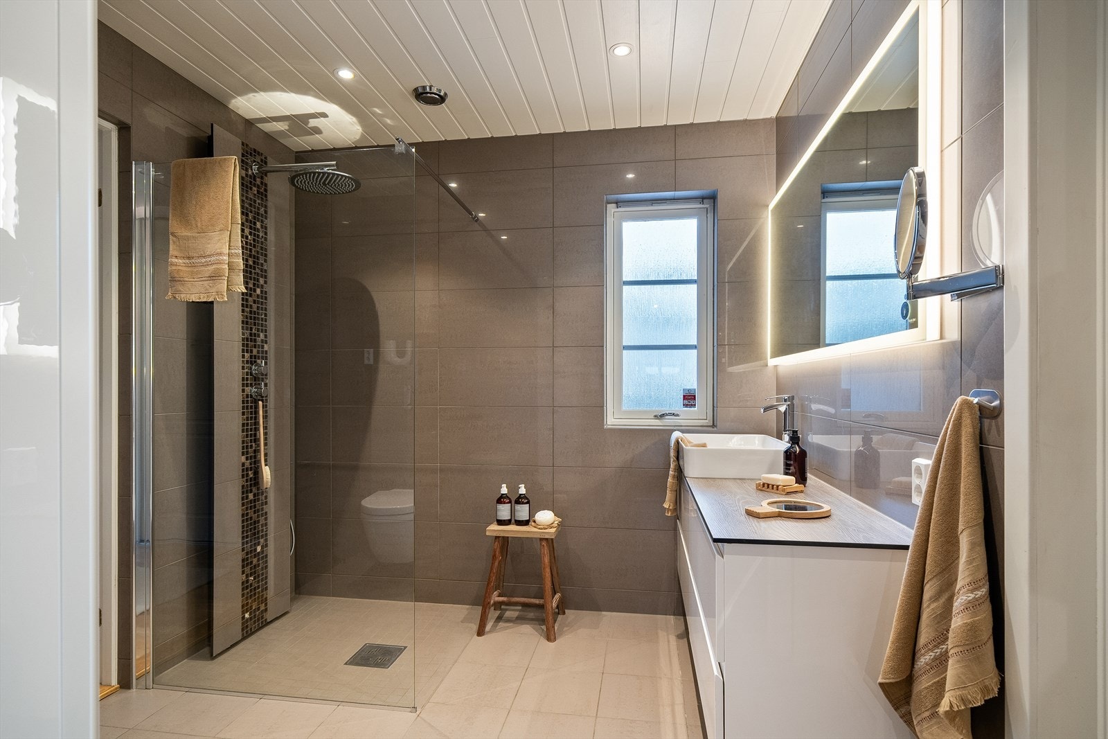 Badet i 1. etasje ble pusset opp i 2018, og har store, gråbrune vegg- og gulvfliser, gulvvarme, downlights og vegghengt toalett Galleribilde