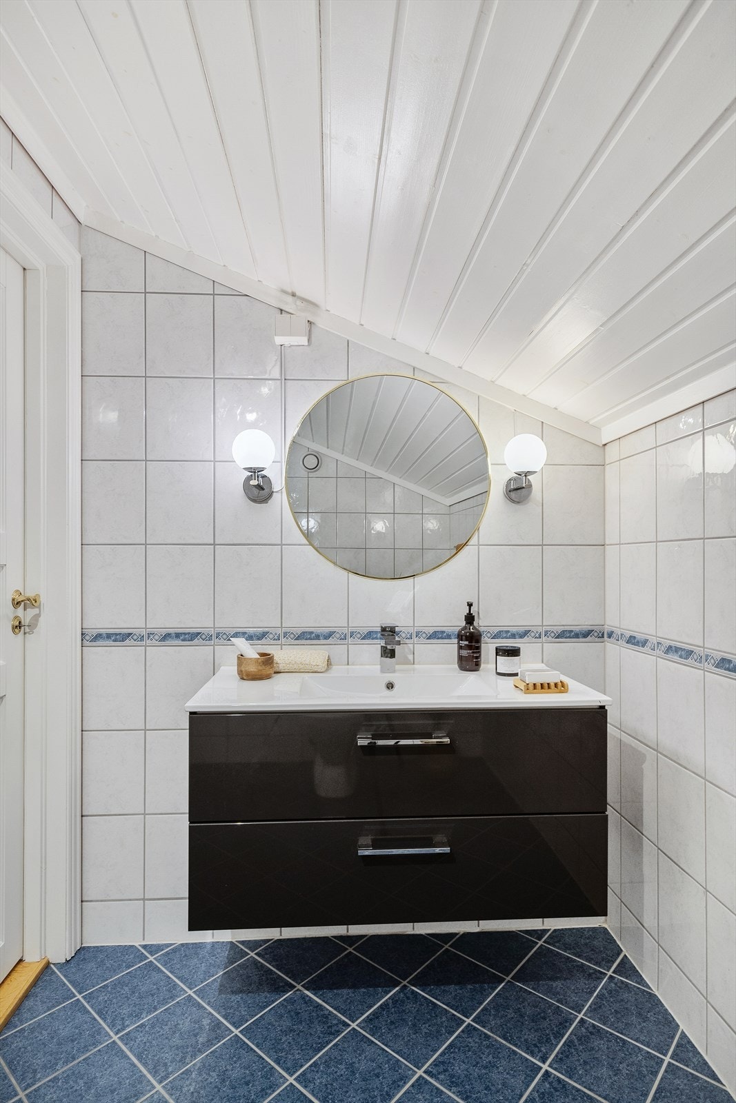 Baderomsinnredningen består av servant med underskap og et rundt speil med belysning Galleribilde