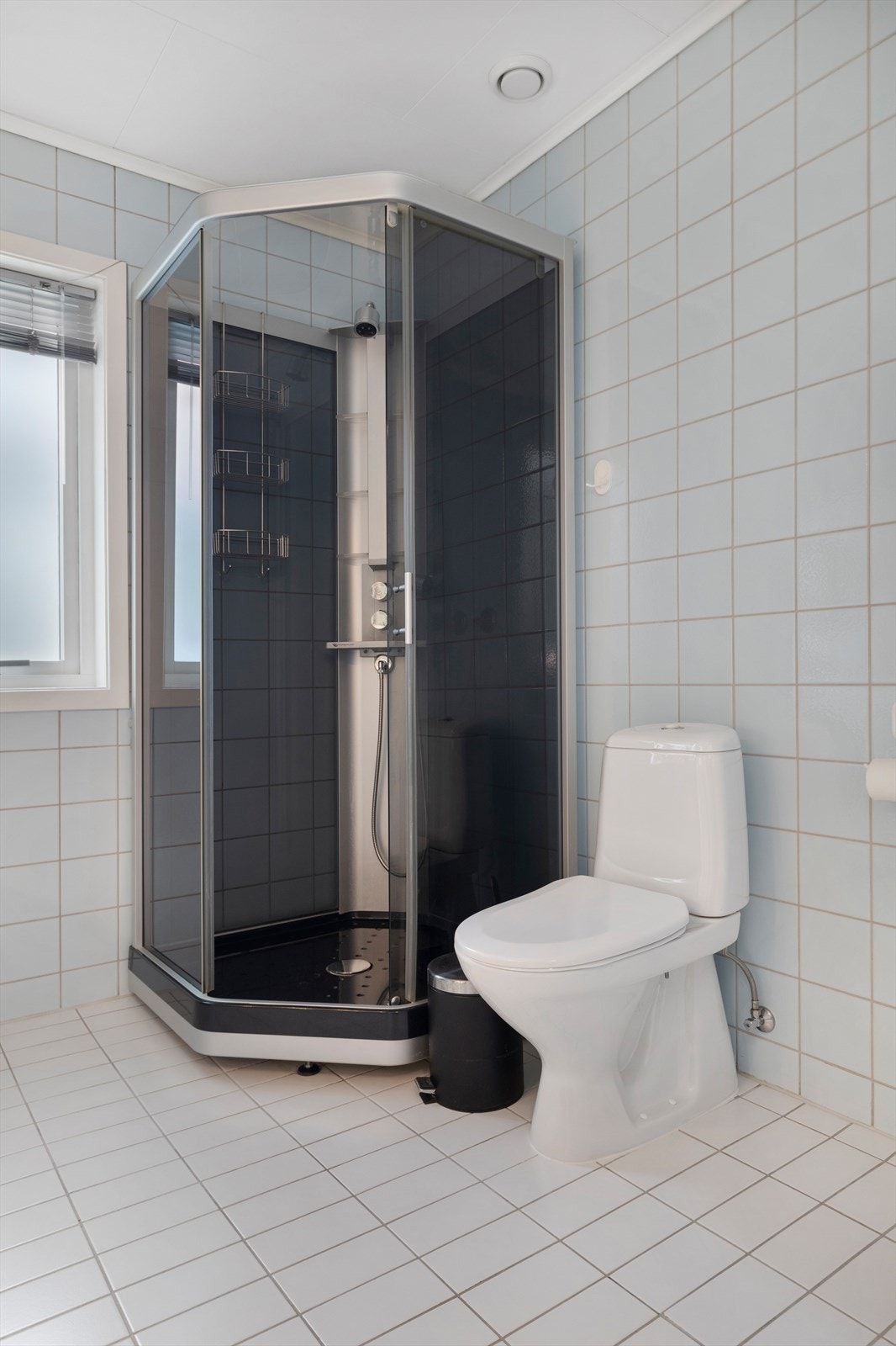 Bad med malte takplater, fliser på vegger og gulv, innredning med wc og dusjkabinett, samt opplegg for vaskemaskin og stikkontakt til tørketrommel. Galleribilde