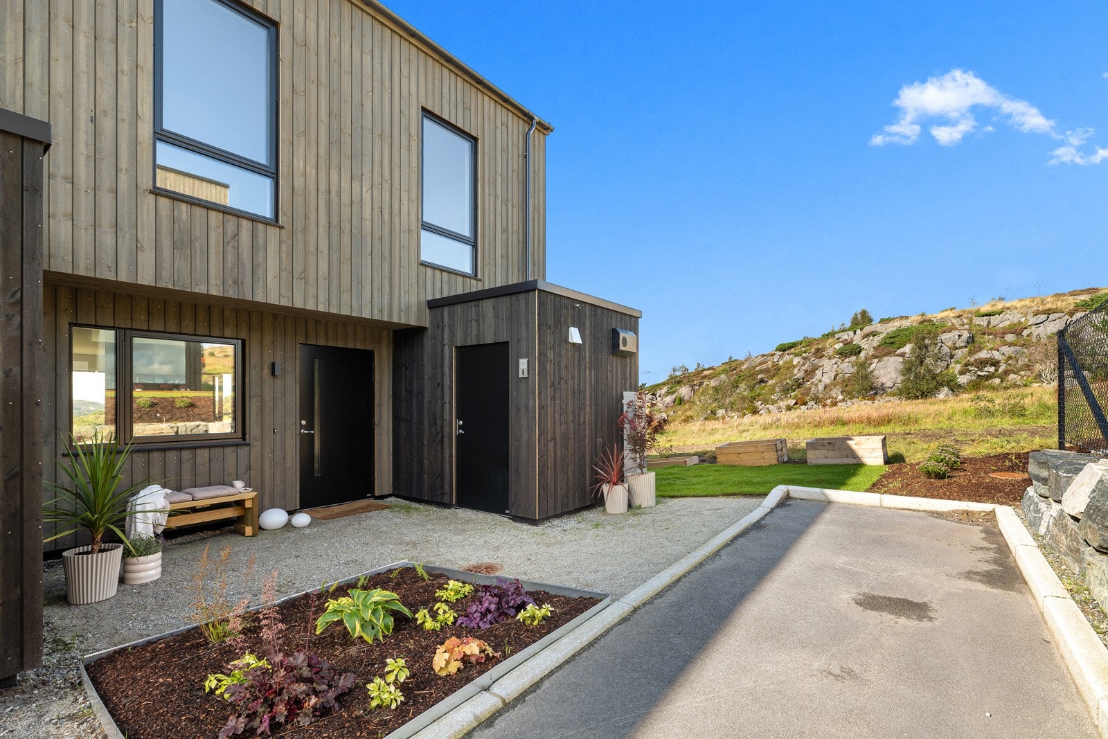 Ved inngangen er det opparbeidet et flott bed for å ønske velkommen til boligen. Selve inngangspartiet er stort og luftig, med plass til både sykler og et koselig kafésett. Galleribilde