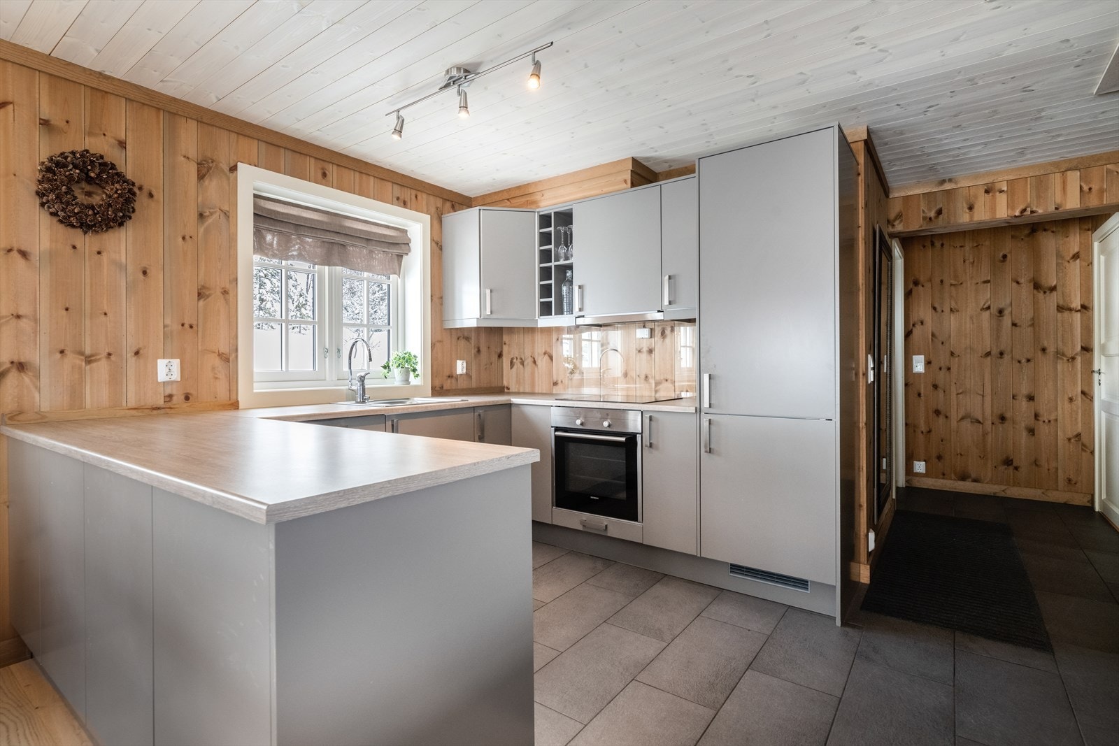 Kjøkkendelen har en pen innredning med slette, lys grå fronter og laminat benkeplate. Det er en hyggelig og praktisk halvøy ut mot spisestuedelen. Galleribilde