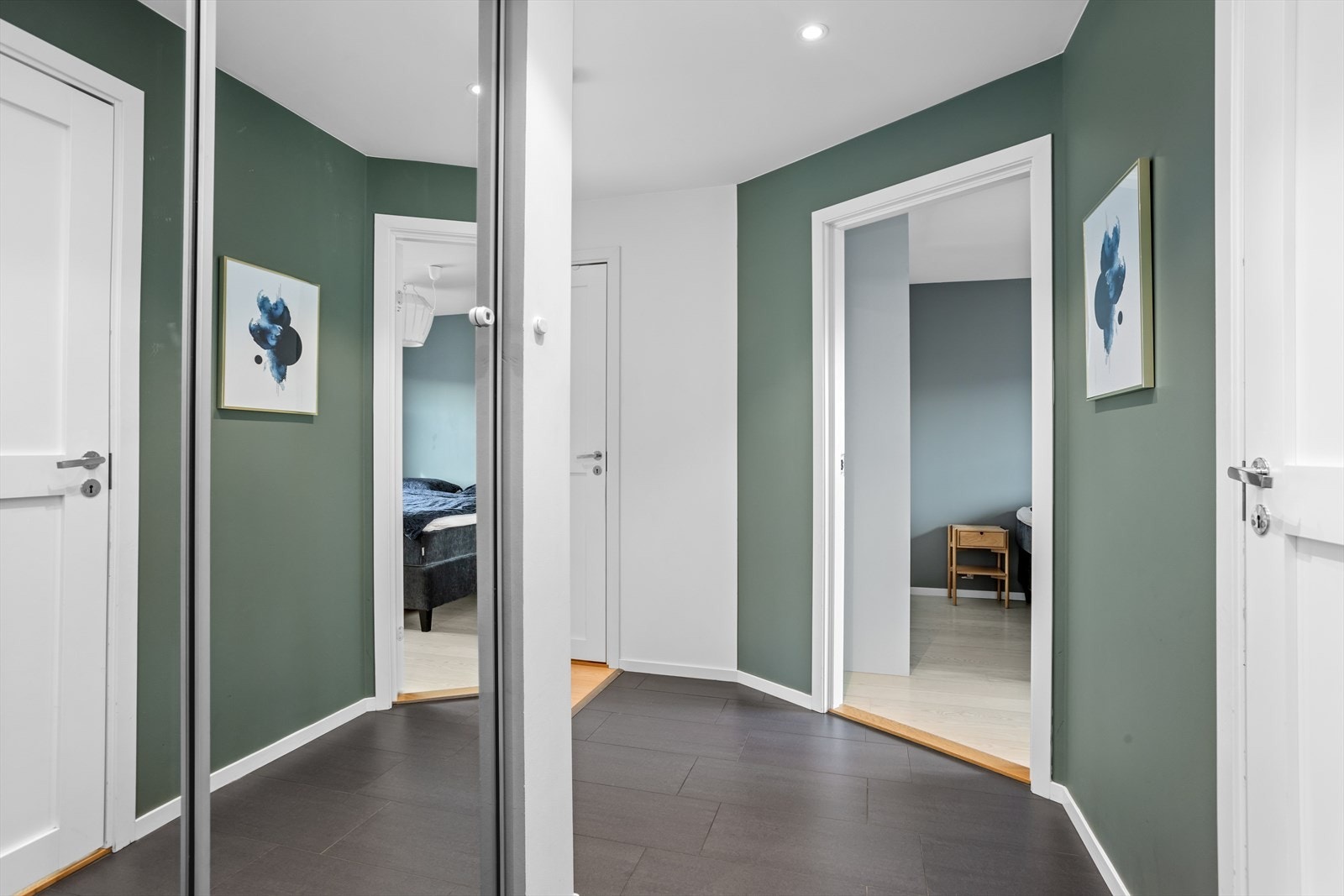 Skyvedørsgarderober bidrar til et ryddig inntrykk. De takhøye speildørene sørger for å visuelt forstørre rommet. Inngangsdøren med smårutede vinduer gir et hyggelig preg til rommet. De slitesterke og moderne gulvflisene med varmekabler gir god varme. Galleribilde