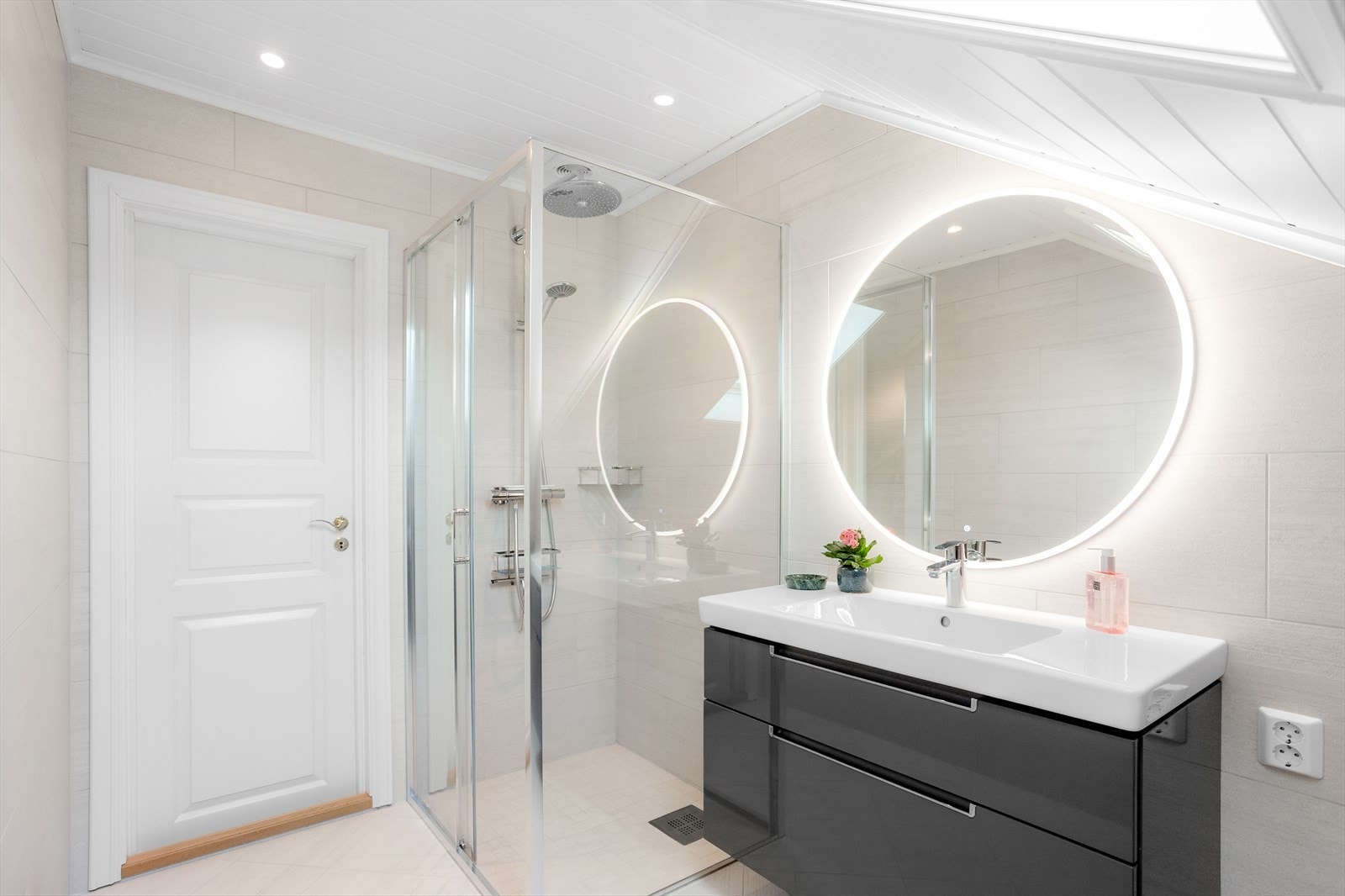 Badet er innredning med nedfelt servant, dusjhjørne, veggmontert toalett og speil med lys. Galleribilde