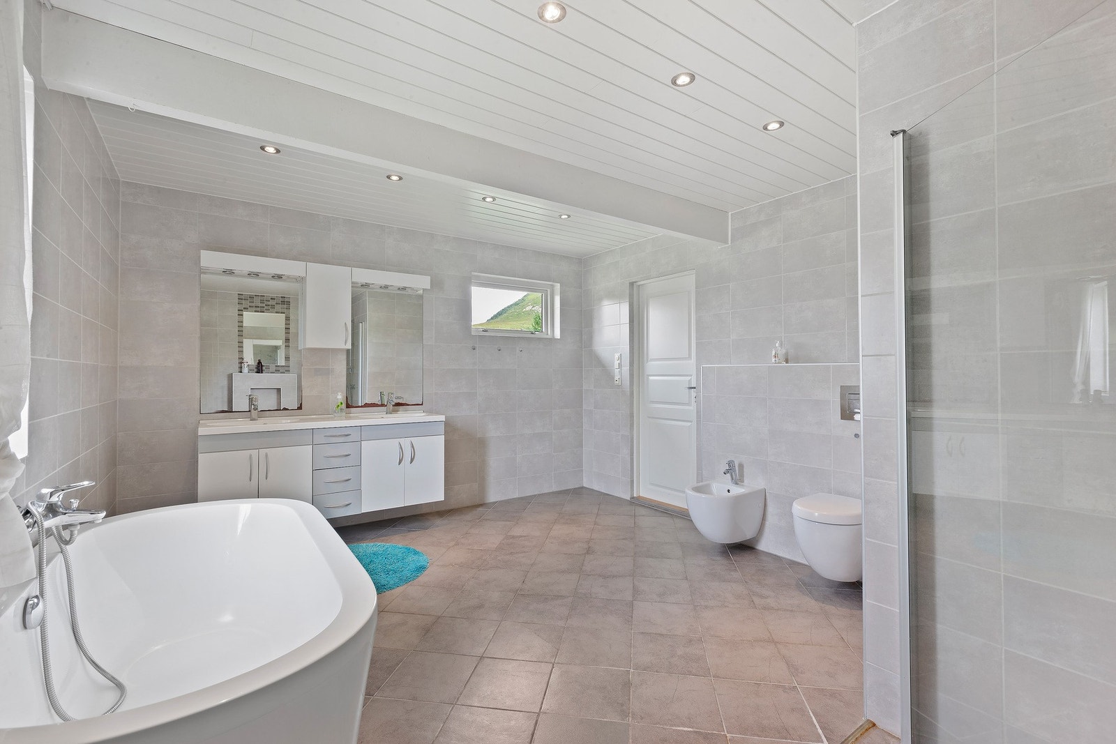 Romslig bad med lys innredning med 2 integrerte servanter med skuffer og skap under, overskap og 2 speil med lys over, badekar, dobbel dusjnisje, vegghengt toalett og bidé, varme i gulv. Galleribilde