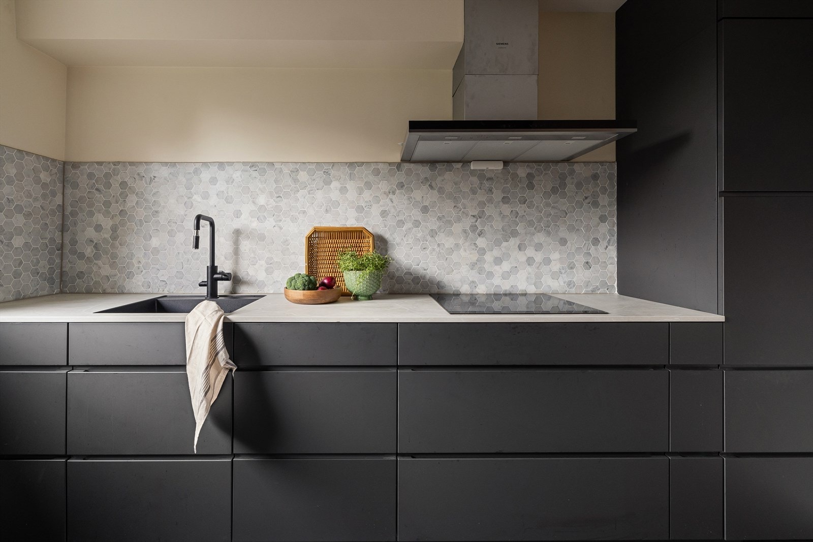 Det sorte, minimalistiske kjøkkenet fra Kvik ble montert i 2022. Hvitevarene er integrerte og bakveggen er flislagt med mosaikk. Galleribilde