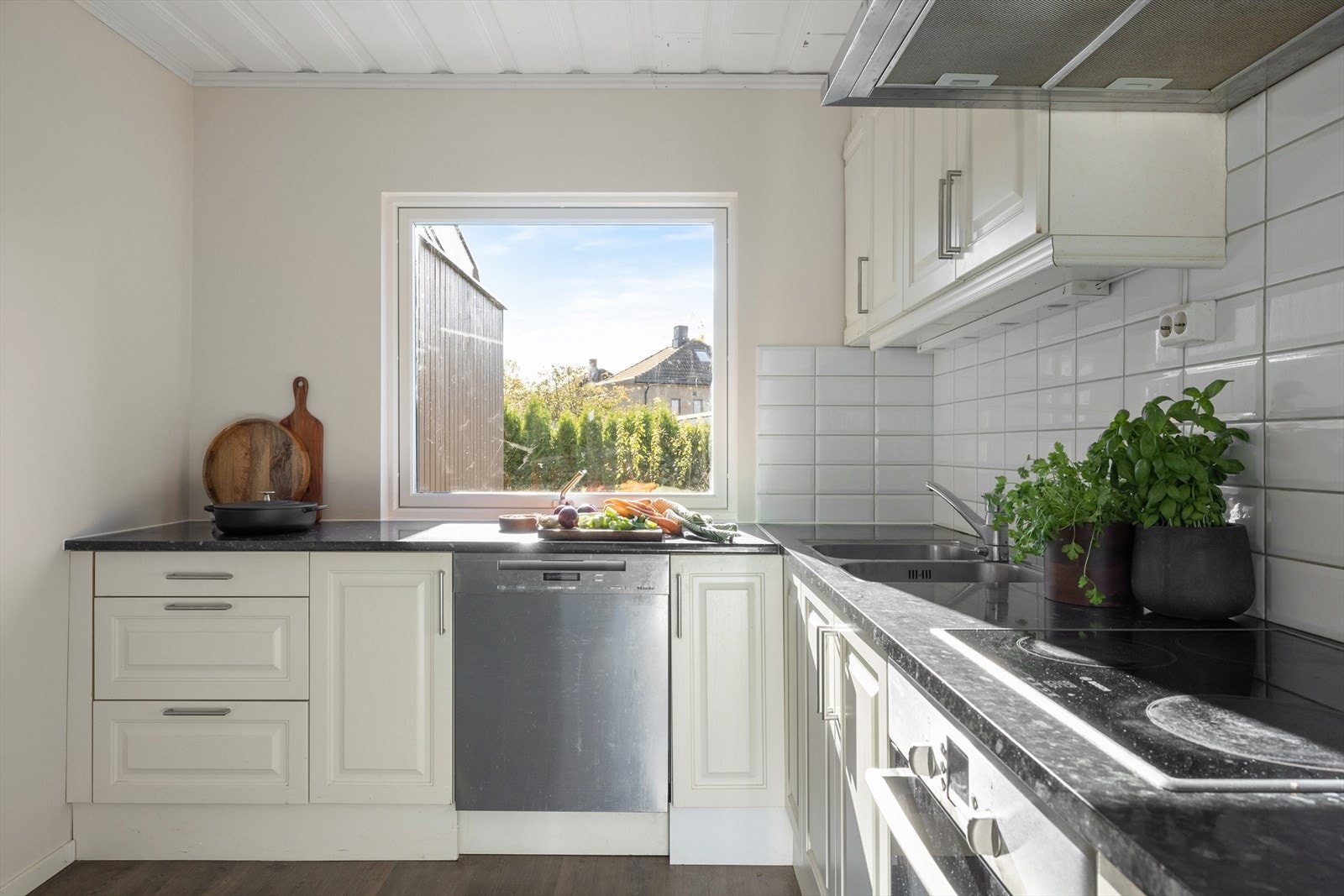 Kjøkkenet har hvite profilert fronter fra 2018 med delvis integrerte hvitevarer og delikat flislegging på baksiden. Galleribilde