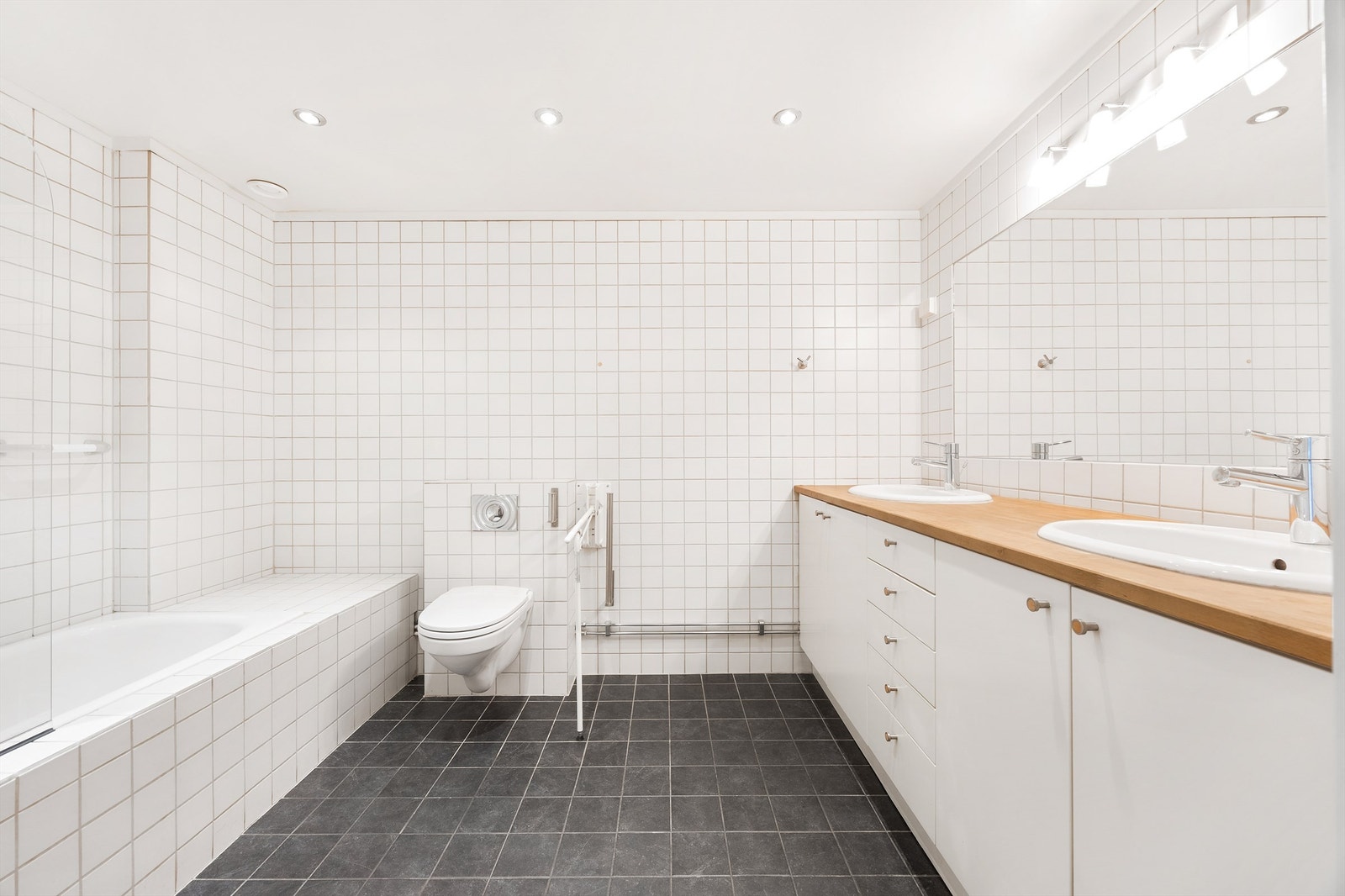 Stort flislagt baderom med dobbel vask i servant, badekar med dusj og vegghengt klosett Galleribilde