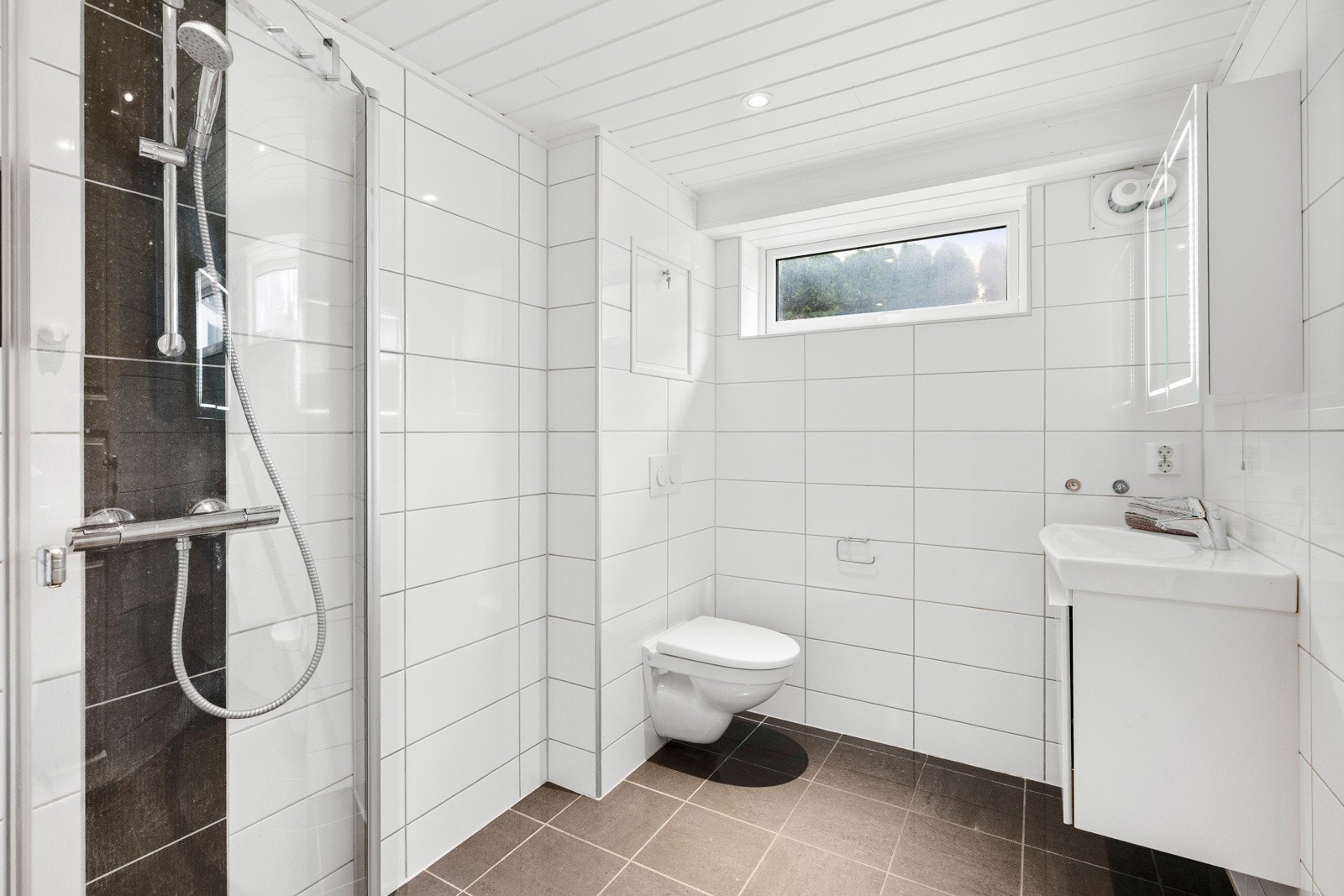 Badet i underetasjen harflislagte vegger og gulv med varmekabler, samt malte plater i himlingen., inkludert dusj med glassdører. Galleribilde