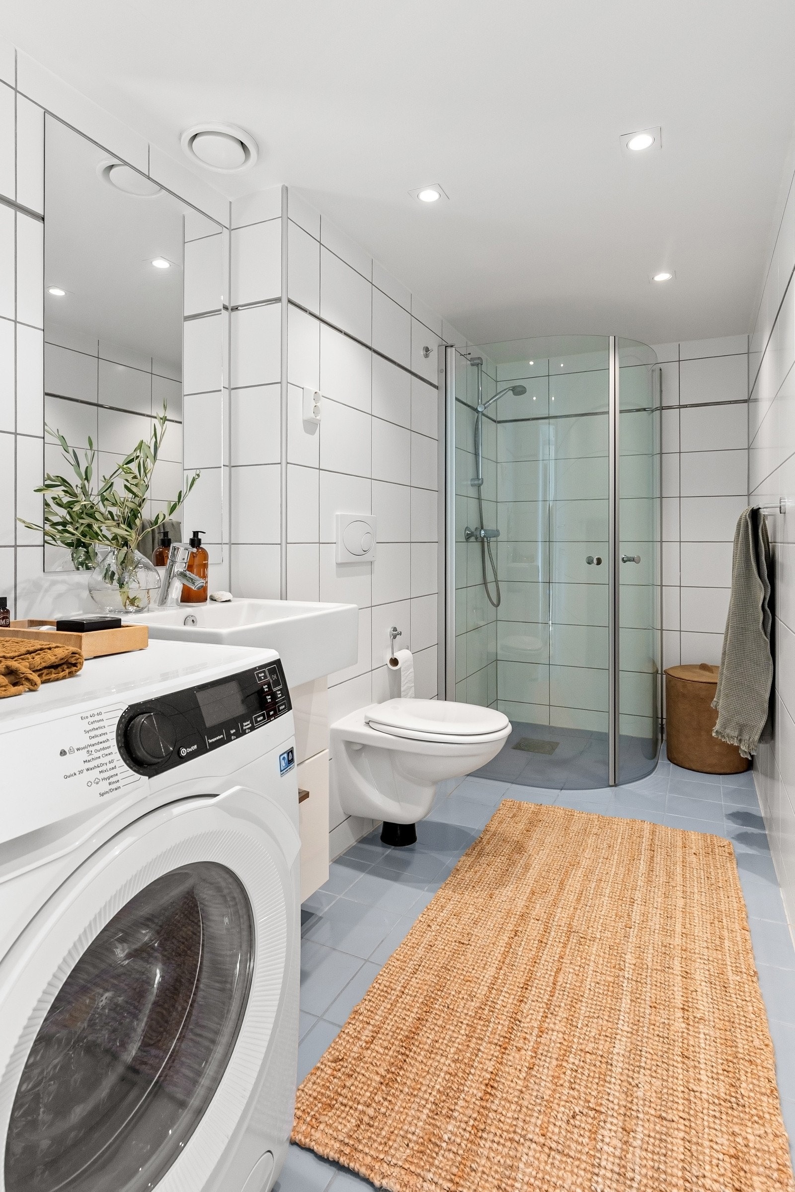 Badet har flislagte overflater, himling med downlights og opplegg for vaskemaskin Galleribilde