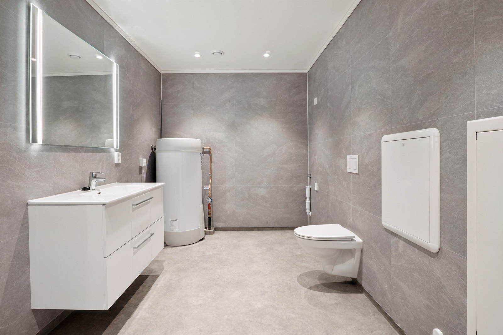 Badet har belegg på gulv og baderomsplater på vegg. Vegghengt toalett og opplegg for vaskemaskin. Vannbåren gulvarme. Galleribilde