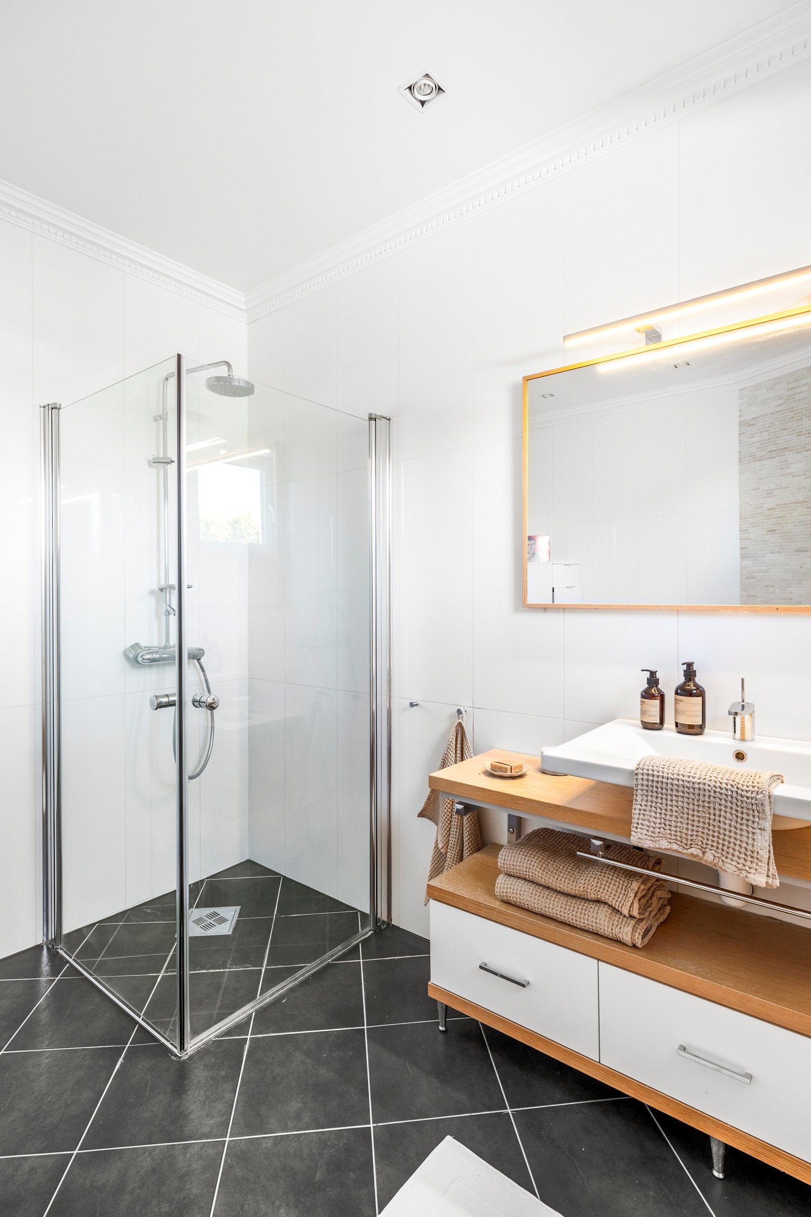 Baderomsinnredningen har hvite skuffer, gylne benkeflater og toppmontert servant, og over er det et stort speil med god belysning. Galleribilde