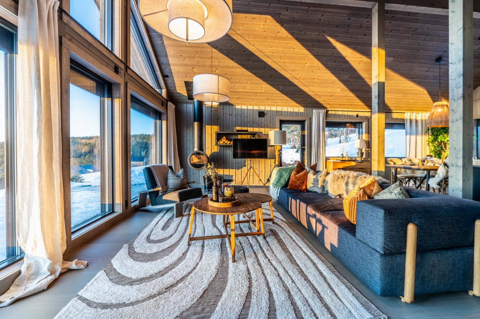 Det er en helt egen stemning i stuen med den flotte takhøyden, utsikten og peiskosen. Peisen heter Ceiling Me og henger fra taket. Sofaen er fra Bolia og pynteputene er fra Home & Cottage og Ralph Lauren. Veggene er beiset i fargen Skigardsgrå. Galleribilde