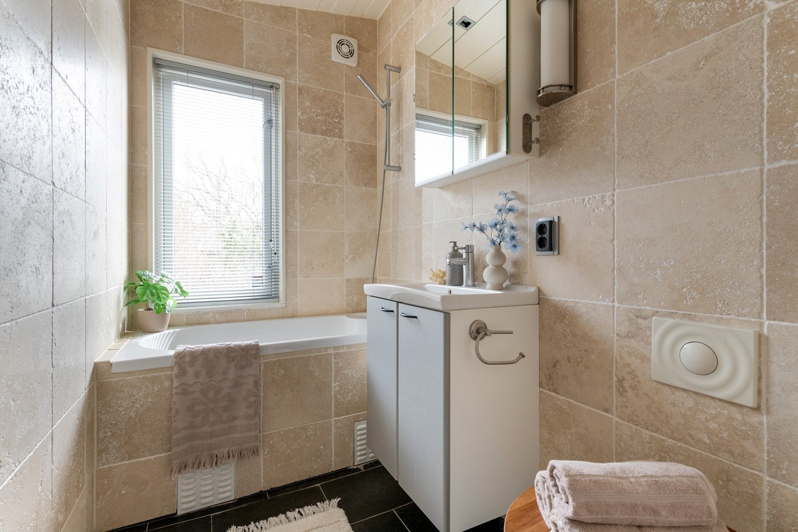 Flislagt bad med badekar, vegghengt toalett og baderomsinnredning med skap, servant og vegghengt speilskap. Vaskemaskin er plassert i lav bod ved siden av badet. Galleribilde