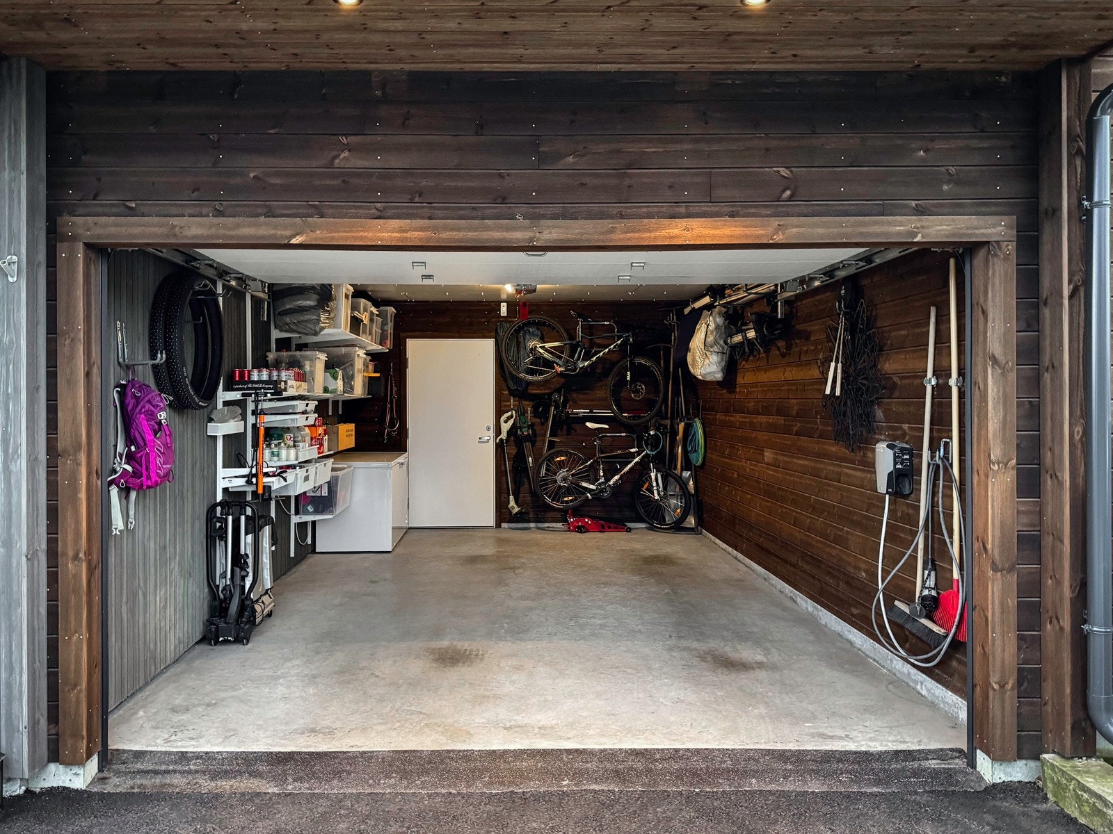 Stor integrert garasje med El-bil lader. Gjennomgang til hagen med dør i garasjen. Parkering for 1 bil i garasje, sykler og 2 biler utenfor garasjen. Galleribilde