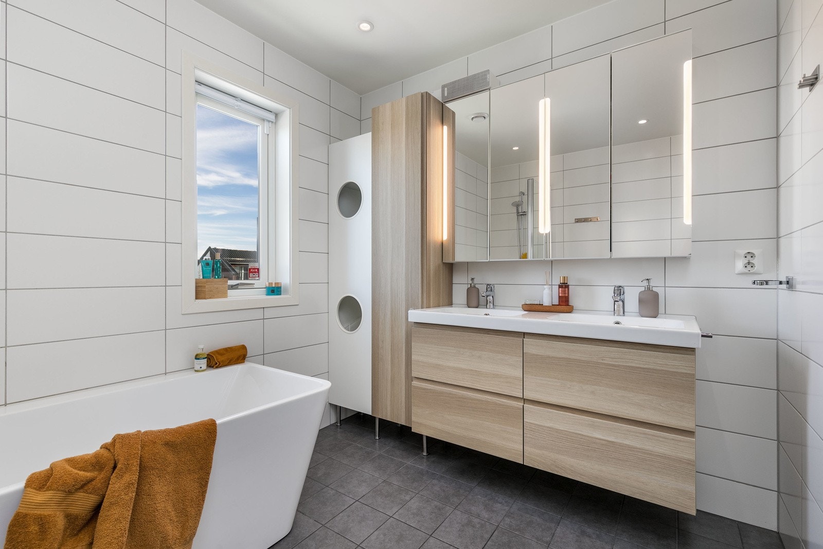 Innredningen på badet består av moderne dobbel skuffeinnredning med dobbel servant og tilhørende speil. Praktisk sideskap sørger for ekstra oppbevaring. Videre har badet et moderne badekar med dusjarmatur og ekstra lang dusjvegg samt vegghengt toalett. Galleribilde