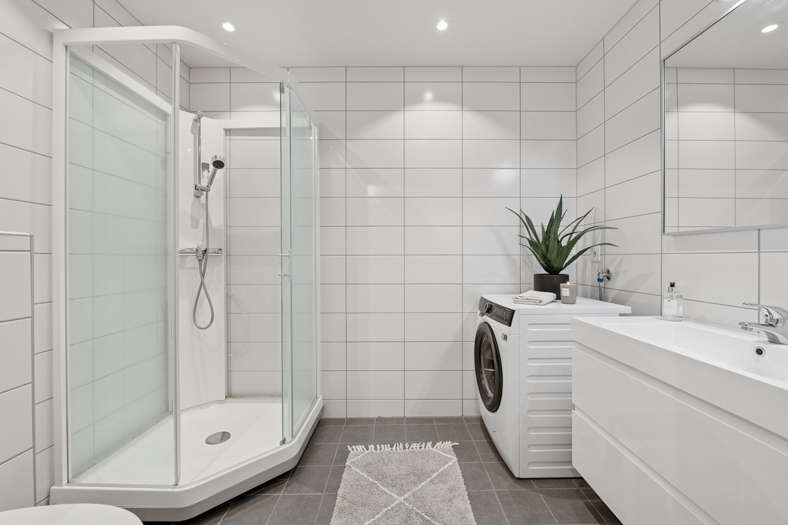 Baderommet fremstår moderne og funksjonelt, med flislagte vegger og fliser på gulv med behagelige, elektriske varmekabler. Taket er malt og har integrerte downlights som gir god og stemningsfull belysning. Opplegg for vaskemaskin. Galleribilde