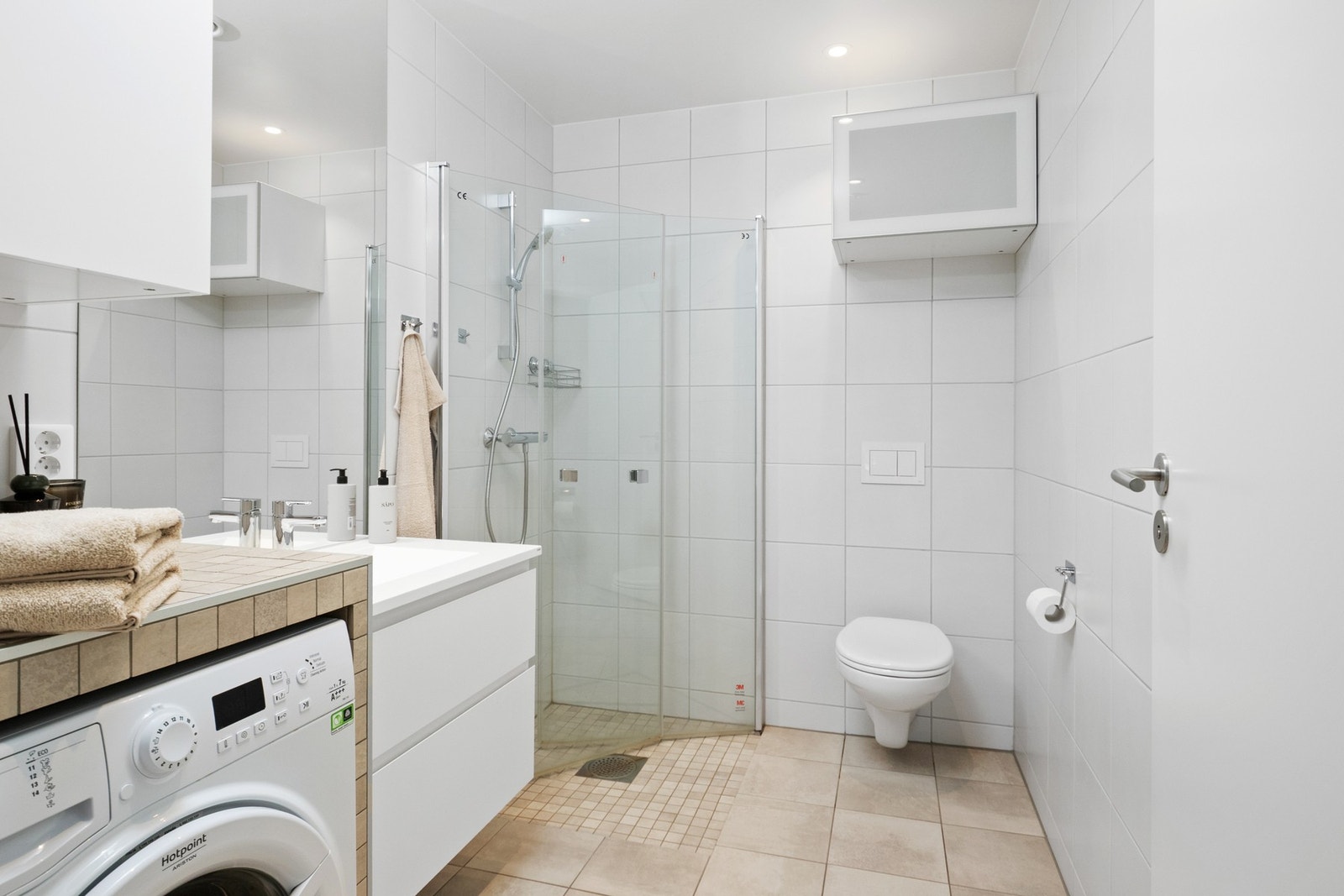 Badet er helfliset og moderne, med vegghengt toalett, dusjhjørne og opplegg for vaskemaskin. Galleribilde