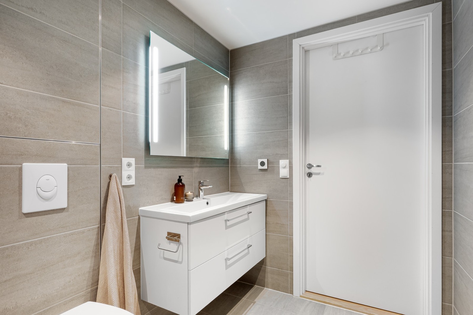 Vegghengt toalett, speil med integrert belysning og en dusjnisje med svingbare glassdører. Galleribilde