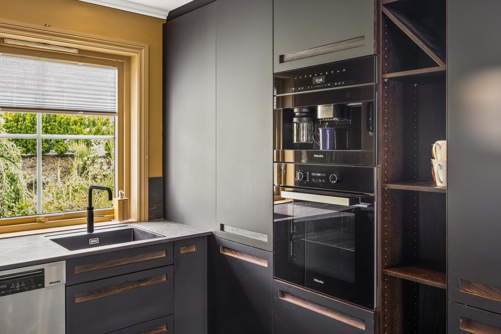 Hvitevarer fra Miele som induksjonstopp, steikeovn, kaffemaskin og matvekt. Frittstående oppvaskmaskin. Benkeplate i stein. Galleribilde