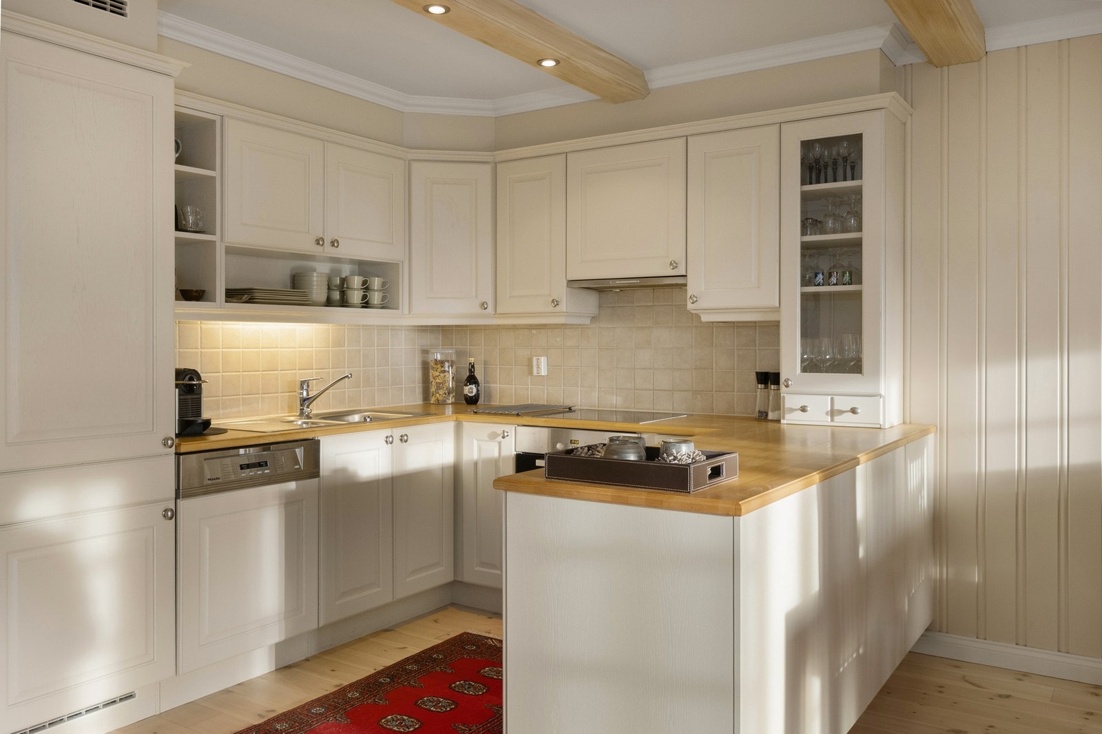 Benkeplate i tre og nedfelt oppvaskkum. Kjøkkenet er godt utstyrt med integrerte hvitevarer: stekeovn, platetopp, oppvaskmaskin samt kjøleskap med fryser. Ventilator er plassert i overskap. Galleribilde