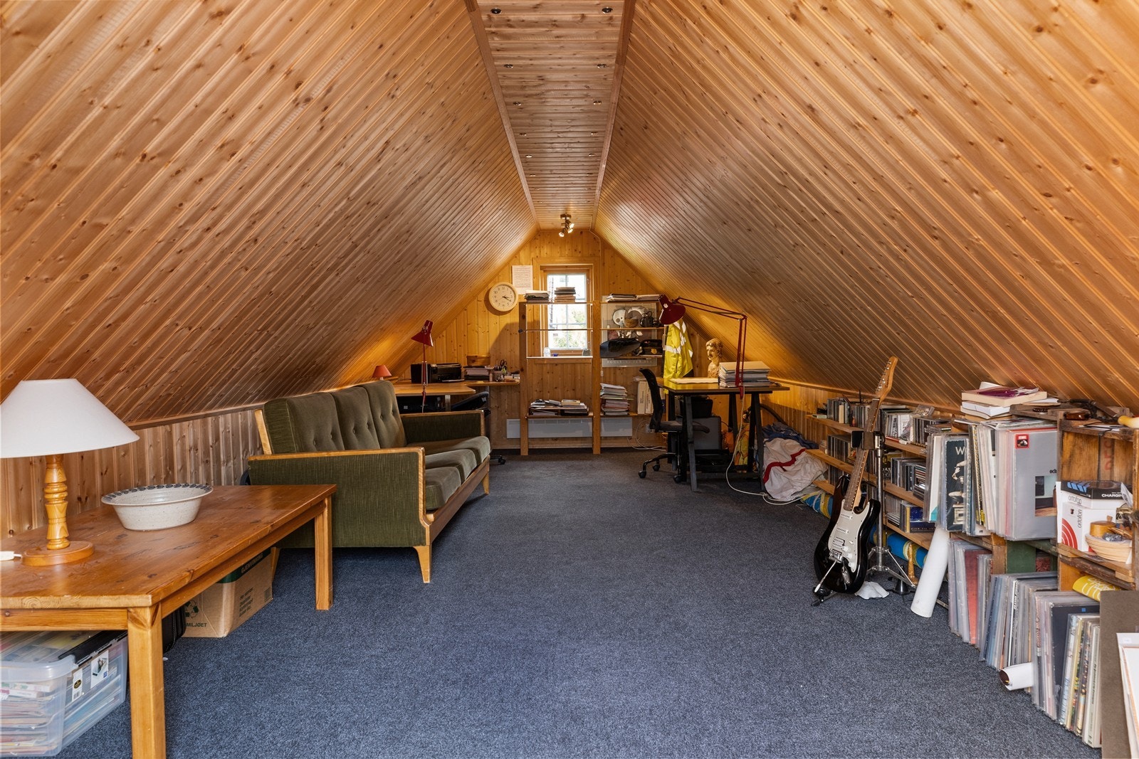 Loftstuen er innredet med gulvteppe, sofa og ulike hyller for oppbevaring. Galleribilde