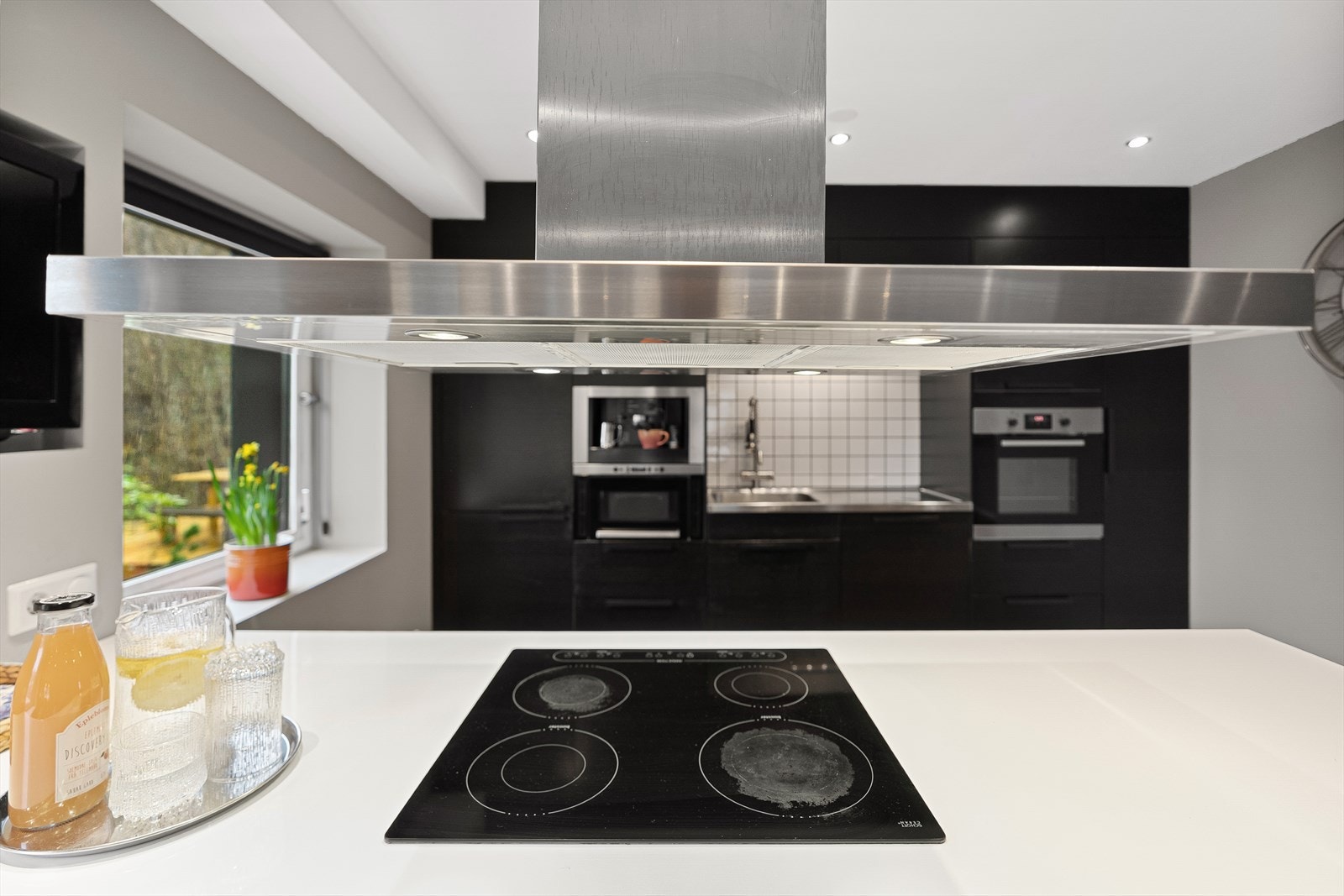 Moderne kjøkken med stilren ventilator og platetopp. Lyse detaljer og store vinduer gir et luftig og innbydende preg Galleribilde