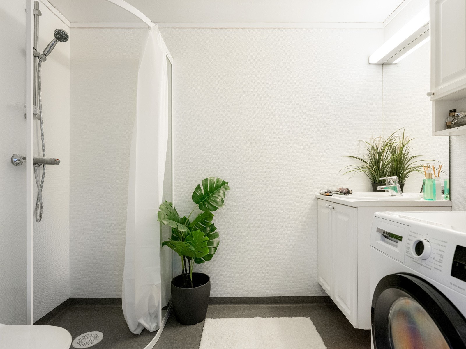 Badet er praktisk innredet med dusjhjørne, servant med underskap og speil, klosett og opplegg for vaskemaskin. Galleribilde