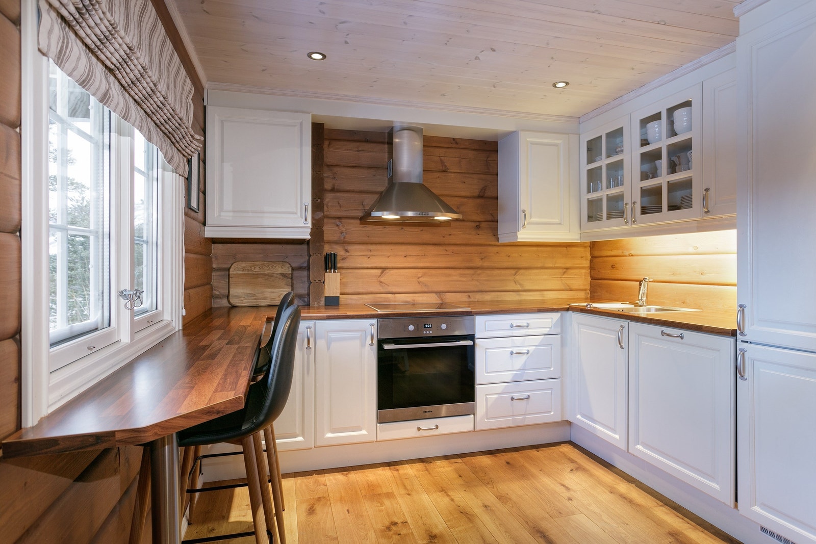 Romslig kjøkken med hvit profilert kjøkkeninnredning med benkeplate av laminat. Det er kjøl/fryseskap, oppvaskmaskin, platetopp og stekeovn. Galleribilde